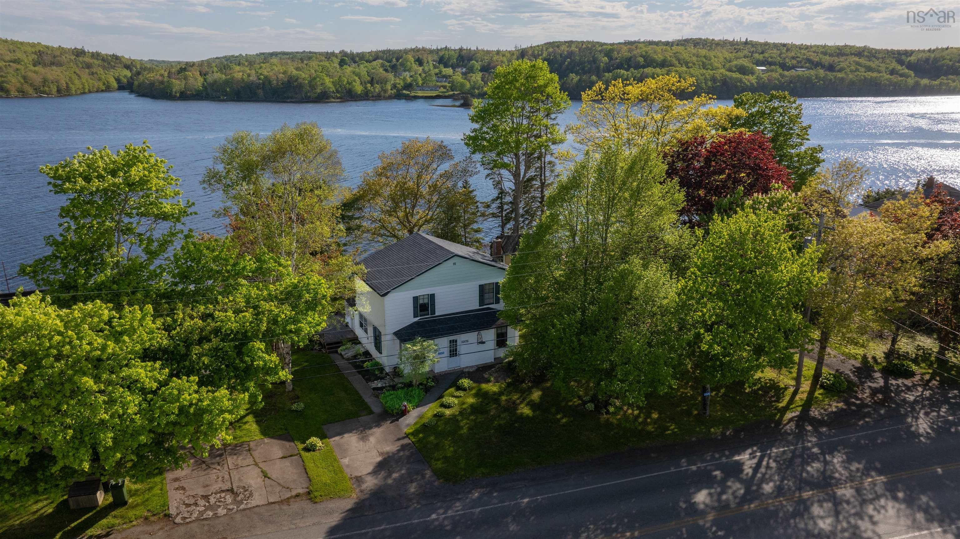 Waterfront property featuring a white two-story residence with a dark roof, surrounded by mature trees