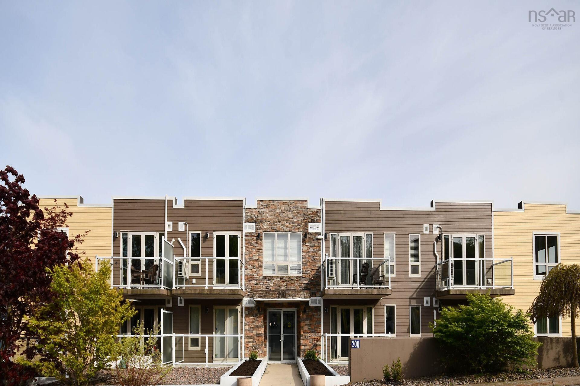 Multi-level residential building with a stone facade accent, brown and yellow siding, glass panel balconies, and multiple windows