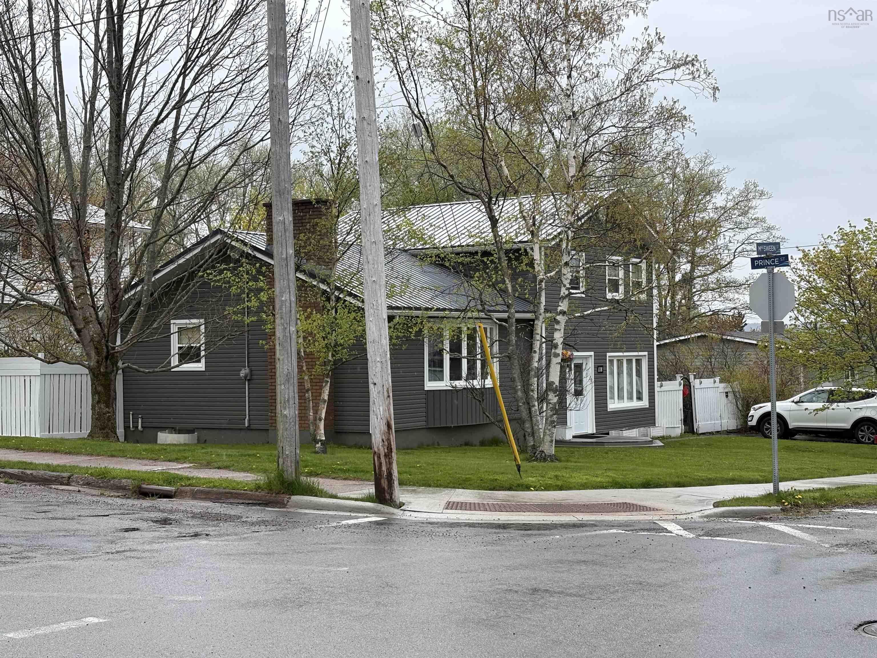 Corner lot property featuring dark gray siding and a light gray roof
