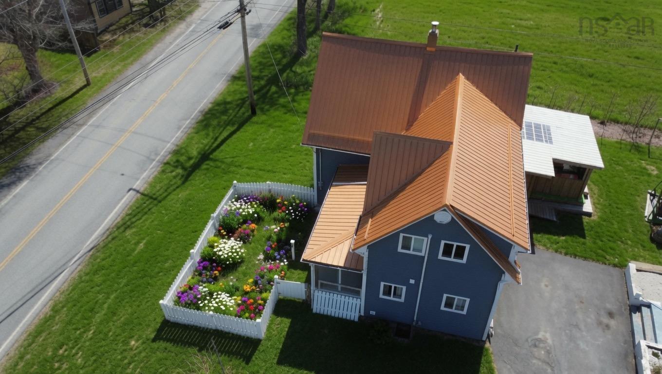 Blue-sided residence featuring a copper-toned metal roof, a white picket fence enclosing a digitaly added flower garden, an attached screened porch, and a paved driveway