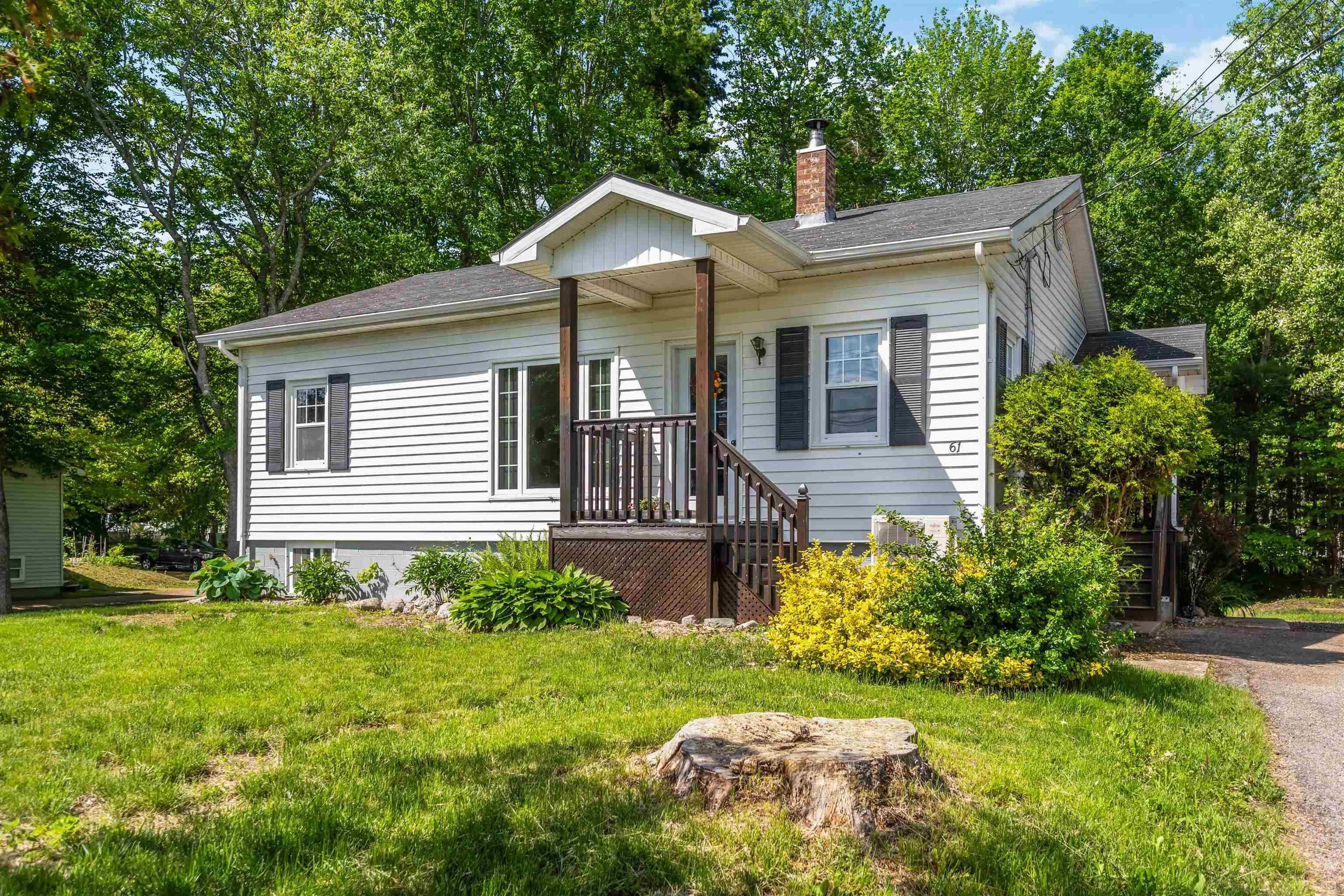 White siding residence featuring a covered front porch with dark wood railings and posts, a dark asphalt shingle roof, a brick chimney, and dark louvered shutters