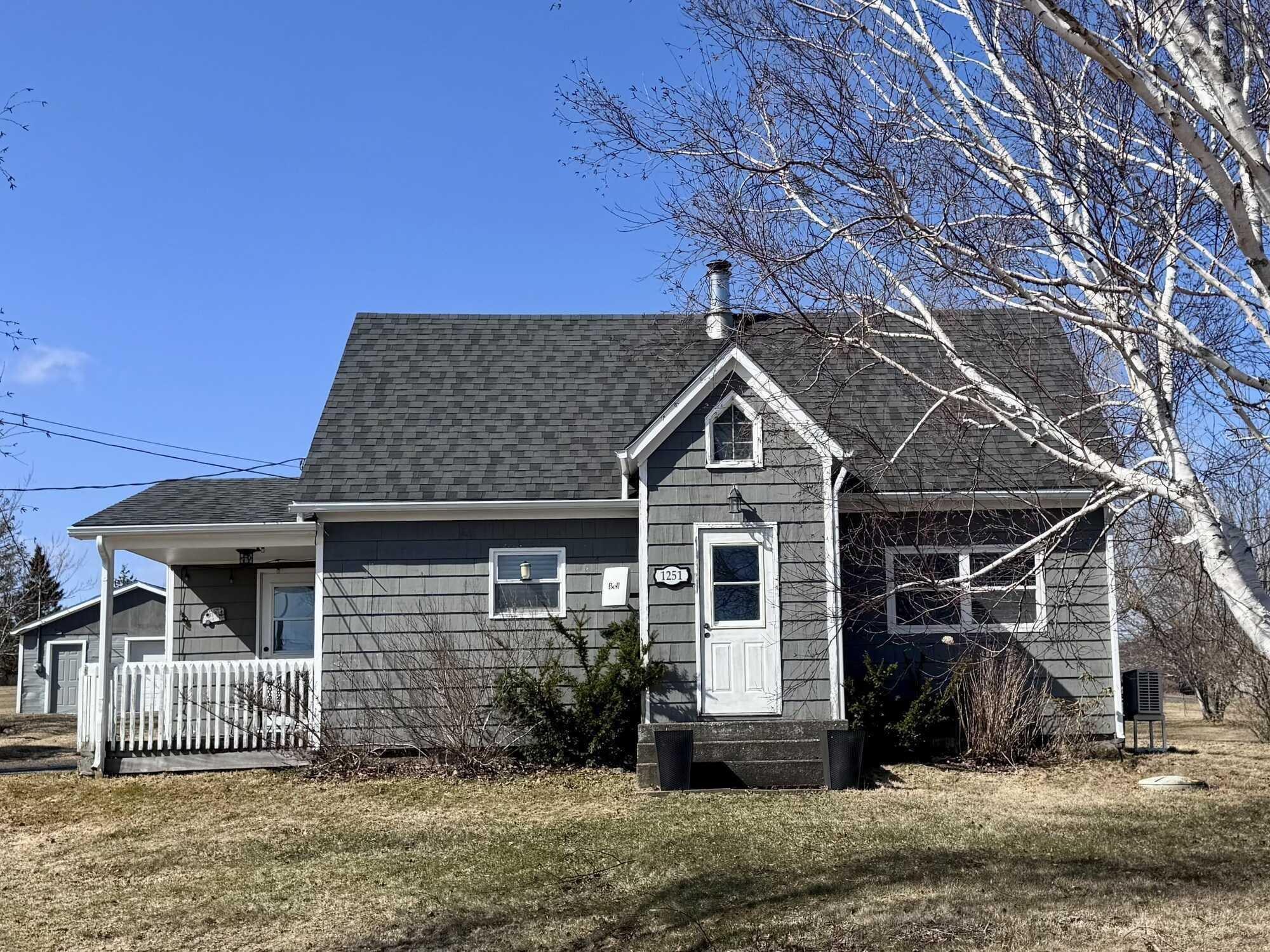 Exterior view of the property featuring gray siding, a dark gray shingled roof, and a white front door