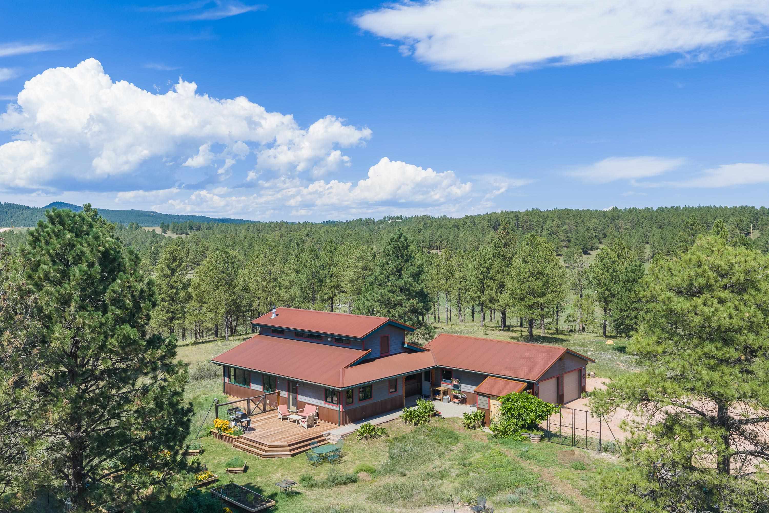 A red-roofed home with a broad wooden deck sits in a pine forest.