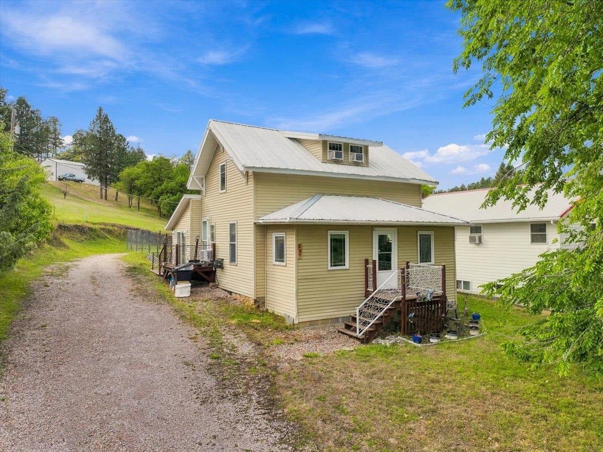 Tan two-story house with a metal roof, raised decks, and gravel driveway.