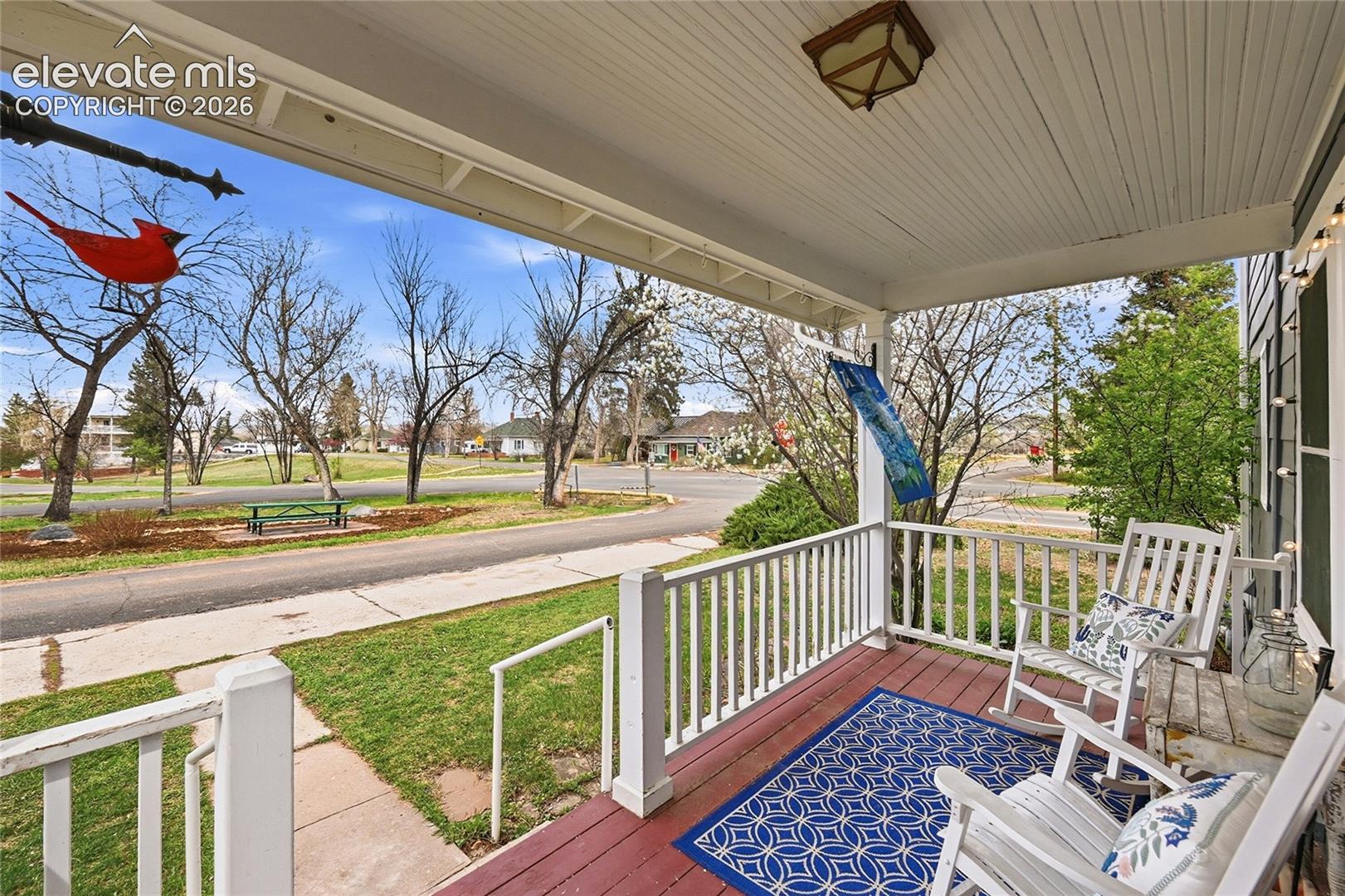 Covered front porch featuring wood-finish decking, beadboard ceiling, white railing, and flush-mount lighting