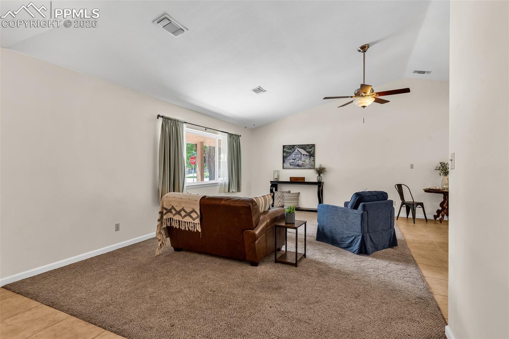 Tiled living area with vaulted ceiling, ceiling fan, carpet flooring, and baseboards
