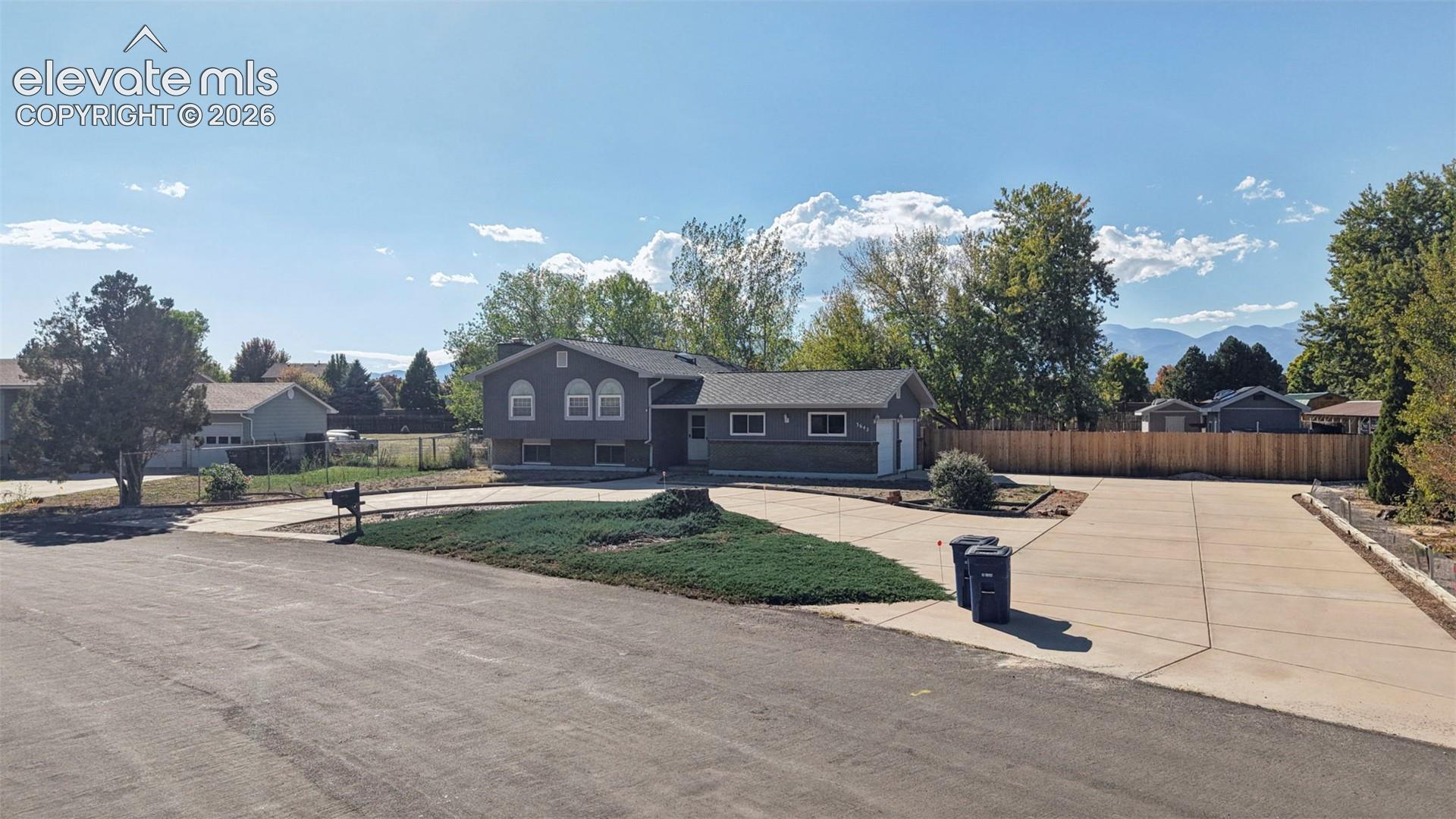 Split-level residence featuring gray siding, a dual-car garage, and a concrete driveway