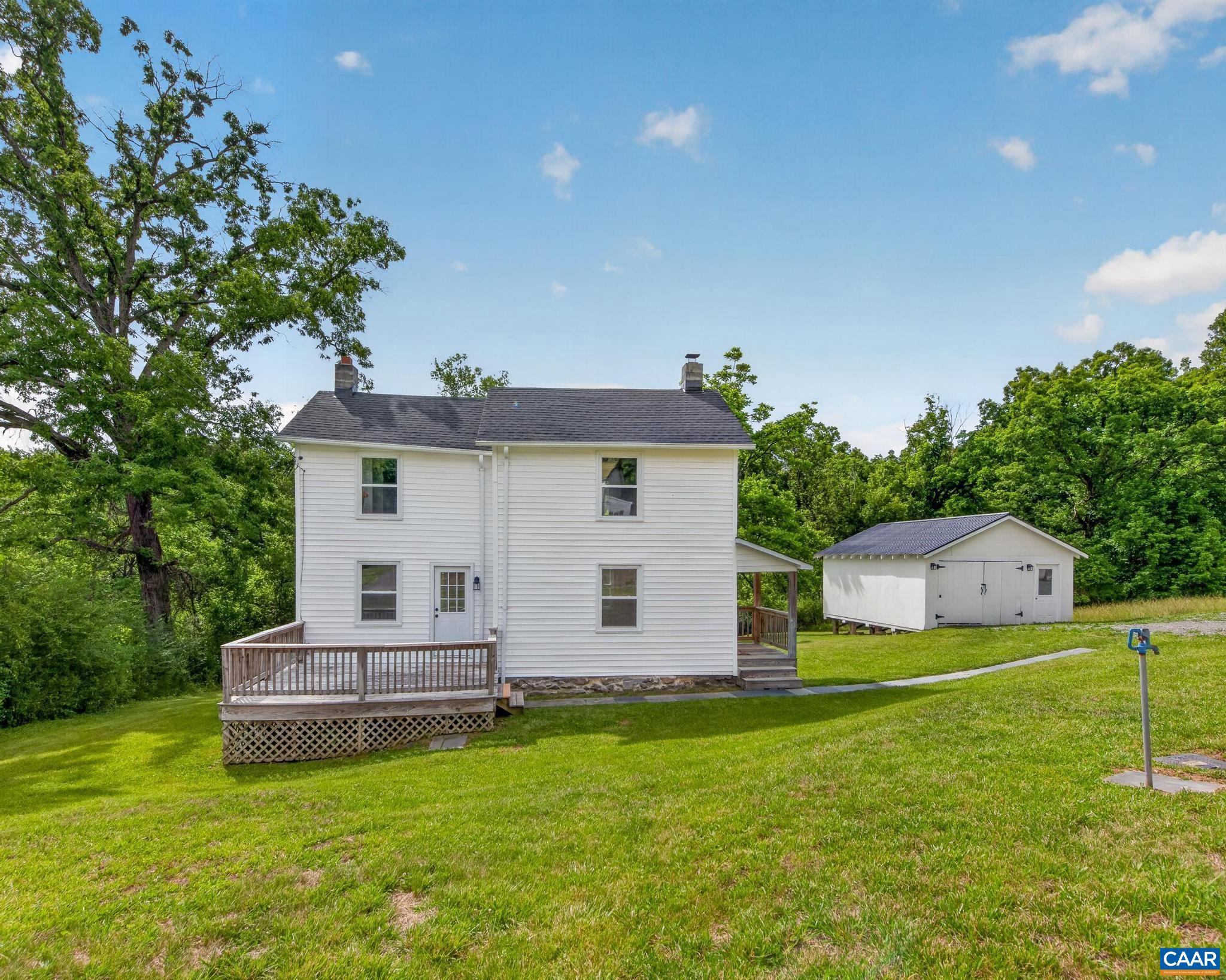White two-story house with a raised wooden deck and detached outbuilding on a green lawn.