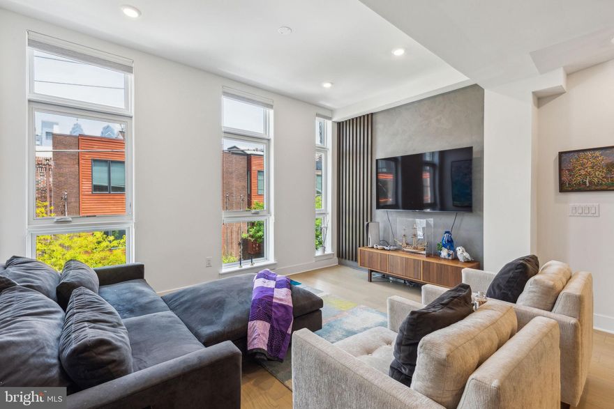 Welcome to the penthouse at Fitz², a fresh and modern 3-bedroom, 2.5-bathroom condo located in the heart of Graduate Hospital. Just two years old, this stylish top-floor residence offers the perfect blend of contemporary finishes and thoughtful design. Enter through a striking glass-enclosed stairway that leads you into the main living level, where Dartmouth white oak hardwood floors and recessed lighting set a warm, refined tone. The open layout seamlessly connects the spacious living and dining areas to a stunning kitchen featuring a white hex backsplash, KitchenAid stainless steel appliances, Grey Carrara quartz countertops, rich Midnight cabinetry, and a large island ideal for entertaining. A generous bedroom with a walk-in closet and full bathroom sits just beyond. Upstairs, the primary suite offers a tranquil retreat with a custom accent wall, walkthrough closet, spa-inspired bathroom, and a private balcony overlooking Fitzwater Street. A convenient powder room leads to the crown jewel: a private rooftop deck with sweeping city views. A third bedroom on the entry level offers flexibility for a home office, guest room, or gym. Perfectly situated near Washington Avenue, South Street, Target, Sprouts, and easy access to I-76, I-95, and public transit—this is Center City living at its best.