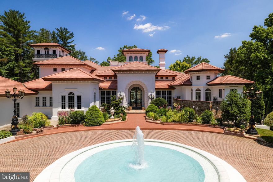 Casa de Amor, or “House of Love,” is a distinguished estate along Potomac’s prestigious Millionaire’s Mile. Set behind stately gates, the residence makes a striking first impression with its Spanish-style red-tile roof, graceful turrets, and a beautifully lit central fountain that draws the eye, especially at night. A paved motor court inspired by Mediterranean villas welcomes guests and leads to one of the Capital Region’s most memorable architectural facades.
 
Inside, custom arched glass and wrought iron doors open to a dramatic interior, where bold onyx floors, softly lit columns, and a carved marble fireplace establish the home’s refined aesthetic. With over 13,000 square feet of living space, the residence was thoughtfully designed using rare materials and timeless finishes throughout.
 
Natural light floods the soaring double-height dining room, while the formal living area showcases a full window wall overlooking the home’s signature feature, a stunning 50-foot indoor pool. Set beneath a glass roof reminiscent of those found in South Beach estates, the pool is surrounded by intricate tilework, palms, and vibrant accents that create a seamless indoor-outdoor feel usable year-round.
 
Nearly every room on the main level opens to the pool area, which also connects to a bright two-story entertaining space with its own commercial-grade kitchen. A dedicated pool bath includes a steam shower framed by detailed mosaics and decorative glasswork.
 
The primary suite offers privacy and comfort, featuring its own outdoor terrace, an expansive dressing room with multiple custom islands, and a spa-inspired bath clad in polished onyx. A richly finished library with dark wood paneling, gold leaf detailing, and a double-sided fireplace opens directly to the pool, as does the main-level wine cellar, a tasteful blend of stone, glass, and contemporary design.
 
More casual spaces include a breakfast room, a two-story great room, and a fully outfitted chef’s kitchen with custom cabinetry and Moroccan-inspired tile. Upstairs, a large sitting area connects to spacious secondary bedrooms, each with luxurious en-suite baths featuring deep soaking tubs and stone finishes.
 
A private glass elevator or spiral staircase leads to the home’s 53-foot observation tower, offering sweeping views across the property and surrounding area.
 
Outside, the grounds feature winding paths, ornate lanterns, and a secluded gazebo, bringing a sense of calm and beauty to the landscaped setting. Every detail has been thoughtfully considered, making Casa de Amor a rare and remarkable opportunity to own one of the region’s most unique and well-appointed residences.