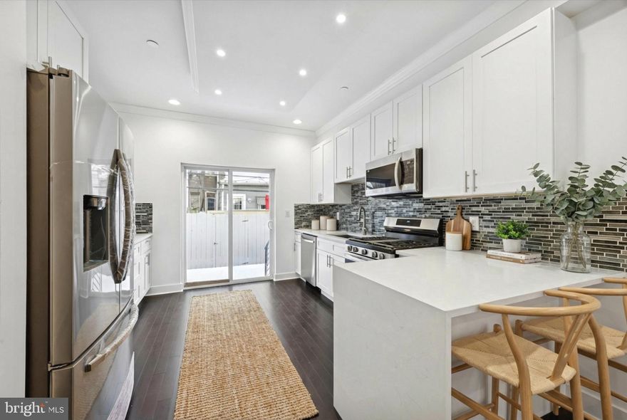 Modern Urban Retreat with Rooftop Views, a backyard with a sliding glass door and a balcony off the primary suite! Welcome to this stunning, new construction home that seamlessly blends contemporary design with thoughtful functionality. From the moment you enter, you'll appreciate the meticulous attention to detail and high-end finishes throughout with stair lights and 3 large full bathrooms! The heart of the home features a bright, open-concept living and dining area anchored by a striking wood-plank feature wall with a sleek modern fireplace. Rich hardwood floors flow throughout, while abundant natural light creates an inviting atmosphere. The gourmet kitchen is a chef's dream with crisp white shaker cabinetry, gleaming quartz countertops, stainless steel appliances, and a stylish mosaic tile backsplash. The spacious island with seating makes meal prep and entertaining effortless, and sliding doors lead directly to your private outdoor oasis. The ground-level patio offers intimate seating perfect for morning coffee or evening relaxation, complete with modern furnishings and privacy fencing. But the crown jewel is the expansive rooftop deck featuring panoramic city skyline views and ample space for entertaining guests under the stars. There is a primary suite off the deck making it a wonderful retreat. Retreat to serene bedrooms featuring contemporary finishes, including one with sophisticated gray tones, floating nightstands, and modern lighting. The bathrooms are spa-inspired sanctuaries with luxurious walk-in showers, elegant tile work, marble countertops, and custom vanities—each designed to provide a hotel-like experience at home. The finished lower level can be transformed into the ultimate entertainment space with a generous rec room featuring modern industrial railings, built-in storage, and room for a pool table, media area, and lounge seating or whatever you envision here. A full bathroom on this level ensures convenience for guests. This new construction home showcases modern finishes in every corner, from the rooftop deck with stunning city views to the spa-like bathrooms with custom tile and marble counters. The finished basement entertainment level provides additional living space, while premium hardwood and tile flooring, modern lighting fixtures, and high-end appliances throughout elevate the home's appeal. The location offers the perfect blend of urban convenience with walking distance to shops, dining, and entertainment. This is more than a home—it's a lifestyle. Schedule your private showing today!