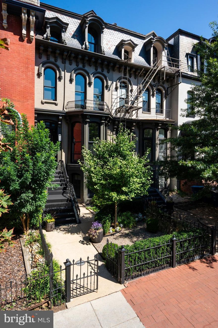 Situated on one of downtown Washington’s most storied blocks, 905 M Street NW is a rare convergence of history, high design, and urban sophistication. Originally constructed in 1865 and newly reimagined by the acclaimed Edith Gregson Interiors, this four-story Victorian rowhome has undergone a comprehensive transformation with significant, thoughtfully executed renovations and custom furnishings. The result is a residence that balances refined architectural character with everyday livability.
 
The distinguished brick façade, accented by oversized Marvin windows and wrought iron detailing, makes a striking first impression. Behind the historic elevation lies a fully modern interior, where soaring ceilings, restored millwork, and wide-plank hickory flooring establish an elegant foundation. Thoughtful enhancements, including custom cabinetry, bespoke lighting, and layered finishes, are unified by a bold, contrasting palette that brings both warmth and an urban edge to the space.
 
The ethereal main level is truly open concept, a sensation only amplified by 14-foot ceilings. Formal and informal living spaces coexist in harmony, subtly defined to accommodate both relaxed living and elegant entertaining. The living room centers on a sleek fireplace wall framed by contemporary built-ins, creating a striking backdrop for large-scale gatherings. The adjoining dining area flows seamlessly into the chef’s kitchen, a showpiece featuring honed black marble counters, an oversized island, an antique mirrored backsplash, and a full suite of Thermador appliances. A moody wet bar provides an elegant nook for displaying fine glassware and enhances the overall sophistication of the space.
 
Ascending the restored grand staircase, the upper levels reveal three gracious bedroom suites, each with a custom walk-in closet and en-suite bath. The primary suite is indulgent, with soaring ceilings and full-length drapery that lends softness and drama, along with a cozy sitting area featuring a fireplace. The spa-inspired bath offers a rainfall shower, double vanity, and private water closet, all unified by a sleek, monochrome palette that evokes contemporary luxury. In contrast, the second suite, currently serving as a private office, is richly layered in deep blues, grass-cloth textures, and brass statement lighting. It includes a wall of custom built-ins designed by Gregson herself. The loft-level third suite features dramatic vaulted ceilings and a lavishly appointed private bath.
 
The fully finished lower level offers versatility with a legal one-bedroom apartment complete with its own private entrance. Ideal as an income-producing rental, in-law suite, or au pair residence, this level is seamlessly integrated into the home’s overall design approach and adds flexibility without compromise.
 
Modern systems include integrated surround sound, a multi-camera security system, and an energy-efficient tankless water heater, ensuring comfort, convenience, and peace of mind. Outdoor spaces include landscaped front and rear gardens, a roof deck with sweeping city views, and two secure off-street parking spaces enclosed by a roll-up gate.
 
Located at the nexus of Shaw and Logan Circle, 905 M Street NW places you just steps from Blagden Alley’s celebrated restaurants, the boutiques of CityCenter, the Walter E. Washington Convention Center, and multiple public transit options. Offering historic charm reinterpreted through a modern lens, this home is a masterclass in design-forward living within Washington’s most dynamic urban setting.