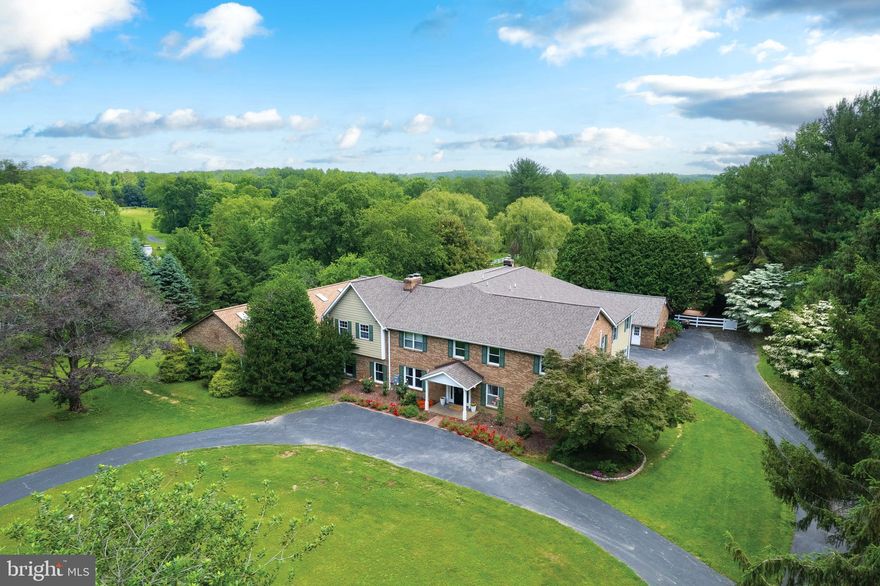 Welcome to 309 Glenville Road, a rare & refined estate resting on 3.3 peaceful acres in the heart of Churchville. With over 8,000 square feet of finished living space & more than $500,000 in carefully executed upgrades, this 7-bedroom, 4.5-bath Colonial has been thoughtfully reimagined to offer an exceptional blend of timeless design, long-term sustainability, and luxurious functionality. Step inside & experience a home that unfolds with elegance and ease. The main level offers both formal & informal living areas, including a front-facing family room, an elegant dining room, a cozy den with fireplace, and a dramatic 31-foot rear living room anchored by a second fireplace. The fully updated kitchen features an induction range, additional hob, new dishwasher, updated cabinetry hardware, and a spacious walk-in pantry combined with a laundry area and newer washer and dryer. A centrally located powder room adds convenience for guests. Twelve rooms throughout the home have been freshly repainted & redecorated with cohesive finishes, new lighting, and carefully selected flooring. This estate features three private en-suite bedrooms, perfectly suited for multigenerational living, guests, or long-term stays. The main-level guest suite offers a walk-in closet, a remodeled full bath, and private access to one of the home’s most striking features: a fully enclosed, climate-controlled indoor in-ground pool with a built-in hot tub section and heating system for year-round enjoyment. Surrounded by skylights, French doors, and full-length windows, this private retreat brings the outdoors in—no matter the season. Upstairs, the primary suite is nothing short of exceptional. Spanning over 800 square feet, it includes two large walk-in closets, dual water closets, a spa-inspired bath with soaking tub, walk-in shower, and double vanity. A connected den offers space for a home office, yoga room, or dressing area. A second en-suite bedroom is privately positioned, and four additional bedrooms,  one  full hall bath, and two bonus rooms complete the upper level—providing space to grow, gather, and create. The lower level offers a full-footprint unfinished basement with over 1,800 square feet of space, ideal for future customization into a fitness studio, media lounge, workshop, or generous storage. Its interior access and large, open layout make it incredibly versatile. Outdoors, the home’s natural setting has been transformed into a true sanctuary. At the heart of the backyard is a fenced koi pond oasis—enhanced by stacked stone, raised planting beds, and two beautifully restored gazebos. The surrounding landscape includes garden electrics, a fire pit area, and winding paths that invite you to wander, gather, and unwind. More than 1,100 feet of pet-safe vinyl fencing fully encloses the backyard, while extensive clearing, landscaping, and planting have restored every inch of the property’s beauty. Efficiency meets innovation with a Tesla-owned, 28.2 kW AC ground-mounted solar array & battery backup. Additional infrastructure upgrades include a new HVAC system, full-house insulation, French drains, open/close AC vents, surge protection, and a whole-home well water filtration system. A wood-burning stove with catalytic converter provides an additional energy source, and the roof has been replaced on the house, porch, and detached garage. Additional features include a two-car detached garage, one-car carport, & a circular driveway with space for 18+ vehicles. An automatic locking dog door with activation tags worn by the pets,  upgraded exterior lighting, refinished back stairs, and a full alarm system with 10 fire/smoke/carbon monoxide detectors—approved by local inspection—round out this move-in-ready offering. 309 Glenville Road is more than a home—it’s a destination. A place where indoor luxury, outdoor serenity, & sustainable living meet in perfect balance.
