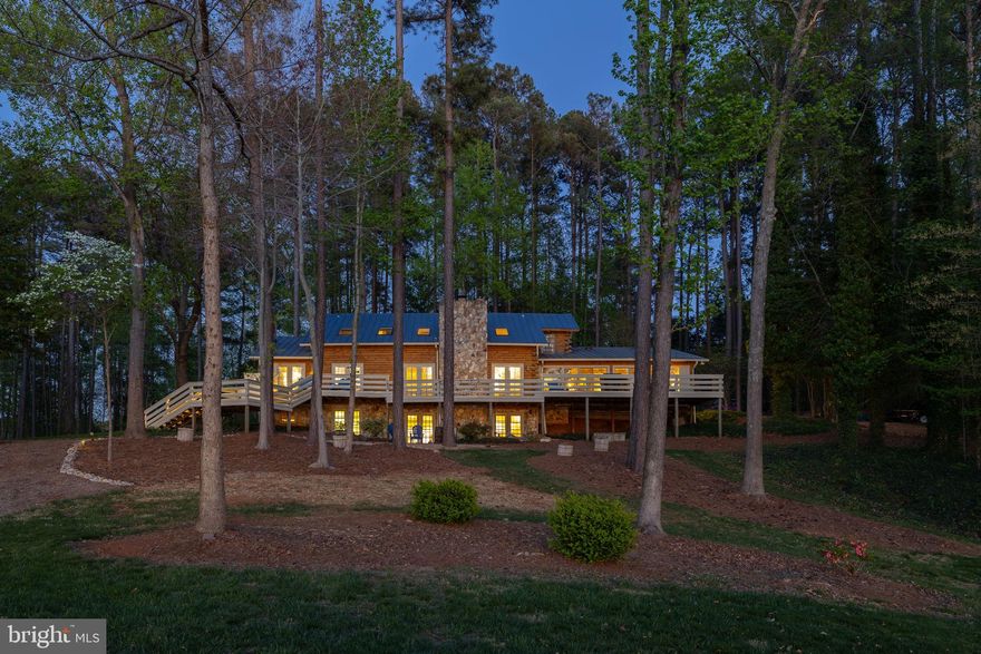 A true waterfront retreat at Lake Anna, Virginia—this extraordinary custom-built log home offers the ultimate in resort-style living. Ideally situated on the southern end of the lake, where the waters are wide, open, and pristine, this property is nestled within the gated Fisherman’s Cove community on the public side of the lake. Offered fully furnished and turn-key, with high-speed Xfinity/Comcast internet available, this is a rare opportunity to step right into luxury lake living. Set on two waterfront lots totaling approximately 2 acres with the potential to build a separate guest house, the property features an incredible 1,300 feet of riprap shoreline and breathtaking western sunset views. Designed for recreation and relaxation, the outdoor amenities are unmatched. Enjoy two boathouses—one featuring two slips with electric lifts, and the other offering a covered slip, cabana, sundeck, and gazebo. There is also a patio for dining down by the water. A waterside sports court is perfect for basketball or pickleball, while multiple fire pit areas create inviting spaces to gather and unwind. Inside, the home is a true masterpiece of craftsmanship, blending rustic charm with upscale finishes. Highlights include 6-inch heart pine hardwood floors, hand-hewn cedar moldings and baseboards, cedar-lined closets, and hand-selected Georgia fieldstone. Three gas fireplaces and soaring vaulted ceilings add warmth and character throughout. A new metal roof (2018), newer upstairs HVAC unit (2022) and two propane water heaters (2025) add peace of mind. The gourmet kitchen is designed for entertaining, featuring custom handcrafted cabinetry, granite countertops, a massive island, a 6-burner gas stove, beverage coolers, a separate prep sink, built-ins, and a stylish wet bar/coffee bar—all seamlessly open to the family room and dining area. The main-level primary suite is a private retreat, complete with a raised gas fireplace, direct access to the full-length lakeside deck, and a luxurious ensuite bath with a soaking tub, separate vanities, a tiled walk-in shower, and a sauna. An additional main-level bedroom offers direct access to a full bath, while a sunroom with sliding doors provides the perfect place to take in the lake views year-round. Upstairs, the loft features a cozy reading nook with built-in bench seating and shelving, along with three additional bedrooms and two full baths. The lower level is designed for entertainment and comfort, offering a spacious family room, recreation area, movie room, full bath, laundry, and storage. Additional features include a paved driveway and a spacious two-car attached garage, offering both convenience and ample storage. Outdoor living continues with a massive back deck, patio, and thoughtfully designed gathering spaces throughout the property. A rare offering on Lake Anna, this one-of-a-kind retreat is ideal as a personal escape, full-time residence, or investment opportunity—short-term rentals are permitted, making it an exceptional find and an even sweeter deal!