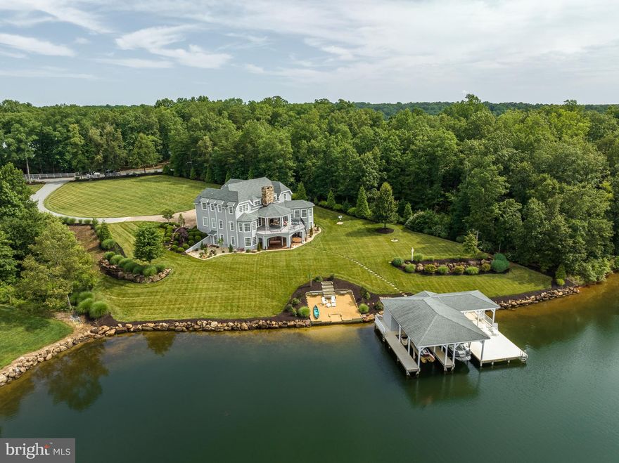 A stunning waterfront masterpiece, this custom oasis offers a spectacular and rare opportunity set upon the beautiful shores of Lake Anna, Virginia. Truly unrivaled in quality and design, this impeccably crafted escape blends modern luxury living with tranquil lake lifestyle. Encompassing over 6,500+ square feet on three open levels, this paradise offers seamless indoor/outdoor lakeside living, with 6 bedrooms, 5.5 bathrooms and a tremendous back deck living area constructed of composite decking overlooking the water that is partially covered with an outdoor stone wood burning fireplace and over 250+ feet of private shoreline down at the water’s edge strongly protected by boulder-sized riprap stones. Step inside into a sunny open floor plan, featuring soaring ceilings with custom beams, two floor to ceiling stone raised hearth fireplaces and gorgeous reclaimed solid wood flooring. Gorgeous views! The bright dining area is open to the gourmet kitchen that supplies stainless appliances, a 5-burner gas stove, smooth quartz countertops, oversized glass pendant lights that levitate weightlessly above the massive island and a large walk-in pantry with custom shelving. The oversized primary bedroom suite is located on the main level, with its own private access to the large deck overlooking the lake, a large walk-in closet and en suite primary bathroom with a stand alone tub, double vanity with marble counters, a separate tile shower and water closet. The other end of the main level includes a half bath, mudroom with laundry and a private second level guest suite with its own bath. Upstairs you'll find a second primary en suite that mimics the main level suite, two additional bedroom, a full bath and a loft overlooking the great room. Downstairs in the expansive walkout basement, you’ll enjoy jaw-dropping effects when you see the oversized raised hearth stone fireplace, wood beam ceiling, and the custom bar with hammered copper sink. There is also an additional room that could be used as a 6th bedroom, a full bath and utility room. This luxury estate is located behind a gate in a quiet neighborhood with High Speed Fiber Internet and no HOA's. Professionally landscaped, lake-fed irrigation, custom paved apron driveway/parking in front of the house and an oversized 2.5 car finished garage. Whole house generator, two tankless water heaters, whole house water filtration and water softener, and Sonos surround sound speaker system throughout the interior and exterior. A few steps away at the water, you’ll enjoy warm summer days down at your private sandy beach and deep water boathouse with composite decking, 2 boat slips (one with an electric boat lift), sun deck, covered area and a storage room (10+ feet water depth at boathouse). Talk about a great central lake location; this oasis is a 5-minute drive from groceries, restaurants and more.  Fox Business recently named Lake Anna THE TOP “beach” vacation investment location in the entire nation - this lakefront paradise would make an incredibly lucrative investment asset and it COMES MOSTLY FURNISHED (see list of exclusions in MLS documents). For those seeking waterfront living at its finest, we offer a private paradise on Lake Anna.