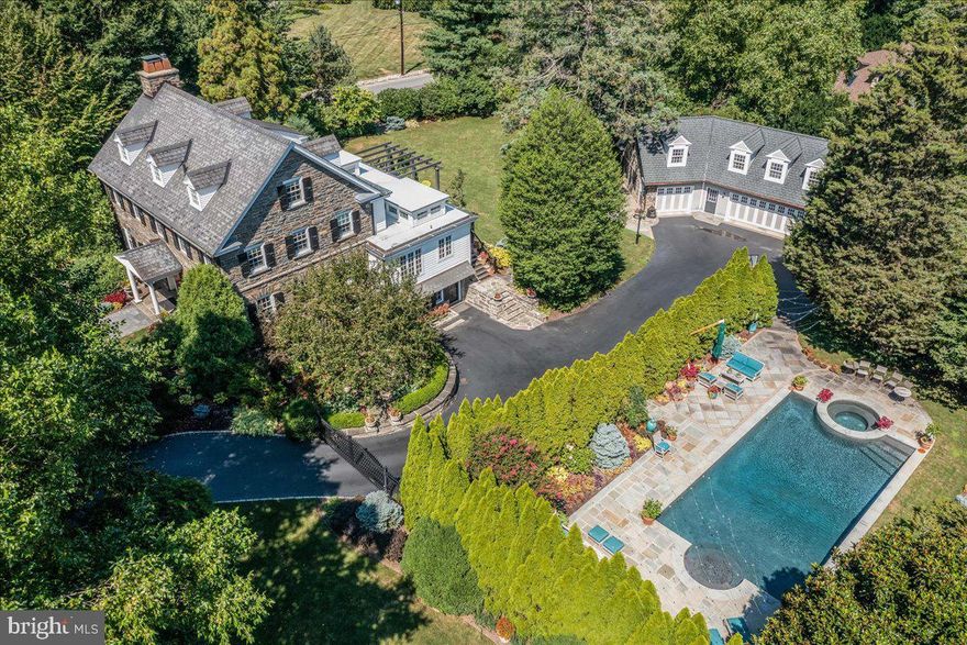 This exceptional home is reverent of the past and poised for enjoyment for many years to come-a signature estate located in Delaware County. The 5 Bed/3.5 Bath Manor House, Carriage House, salt water pool, and spectacular grounds are flawless. The owners have meticulously engaged master craftsmen to create a home suitable for the most discerning Buyer. Every room speaks of fine quality renovation with classic finishes. This home is ideal for entertaining on a large scale, including hosting fundraising events, enjoying tranquil evenings by the classic swimming pool, or roasting marshmallows over the gas fire table on the deck. Once inside, you immediately feel that this house will beguile you with its quiet elegance and comfortable surroundings. The Formal Living Room features a gas fireplace with a large antique nineteenth century white pine wooden mantel and handsome built-in shelves. The ambiance of the elegant Dining Room is enhanced with hardwood flooring and custom shimmering cork wallpaper, chair rail, crown molding and wide window sills. The exceptional culinary Kitchen was completely renovated in 2015. High end appliances include Wolf gas cooktop and oven, Dacor warming drawer, Sub-Zero refrigerator and Miele dishwasher. The oversized range hood provides architectural interest along with a large display shelf. Filled with natural light, the Kitchen is warm and inviting with Downsview white cabinets with black granite countertops and a contrasting dark cherry wood island with handsome Calacatta Gold marble top. The unique clerestory windows fill the space with sunlight and give this room a feeling of luxury and prominence. The Butler's Pantry features a hammered copper sink, Calacatta Gold marble countertop, custom cabinets (some with glass inserts), a wine refrigerator and service stairs to the second level. The extraordinary Family Room is filled with natural light through clerestory windows, and is accessed either from the Kitchen or through glass inset French Doors to the Living Room creating a pleasing flow. This room is enhanced by an impressive exposed stone wall, custom built-in cherry cabinetry and oversized windows that provide exquisite views of the lush surroundings.  Radiant heat warms the California Gold mixed natural slate floor. A Mudroom and Powder Room complete the main floor. The Primary Bedroom with hardwood floors is spacious and provides tree top views. Step down into the luxury of the custom designed Primary Bathroom, featuring a steam shower, water therapy soaking tub with air bubble jets, double sinks with quartz countertop, cherry cabinetry and a private WC. This oasis of relaxation is warmed by heat lamps and a radiant heated tile floor. The 2nd and 3rd Bedrooms both have a charming ambiance with corner gas fireplaces and attractive ash colored wood floors. A bright and charming hall bath is enhanced with white tile floors, a hand painted Italian sink, white cabinets and linen closet. The third level provides additional ample living space with two more attractive Bedrooms, a full Bathroom, and two walk-in cedar closets. The finished basement includes, Laundry, Storage, and a work and recreation space.  For peace of mind, there is a generator which powers about 90 percent of the property. The 3 car Garage has heat and A/C, with Carriage House above. The Carriage House offers a large Living Room, Kitchenette with dishwasher, microwave, sink and under counter refrigerator, full Bath and spacious Bedroom. The heated, salt water Pool and Spa is surrounded by magnificent gardens with dramatic lighting, flagstone walkways, a pond with a fountain, and circular stone patio–perfect for dining al fresco. Beyond the pool is a fenced area for your beloved pets to enjoy the outdoors safely. The property is unparalleled with exquisite gardens creating a fabulous and inviting outdoor environment. Conveniently located just steps to the train to Center City, schools, parks, and close to dining and shopping.