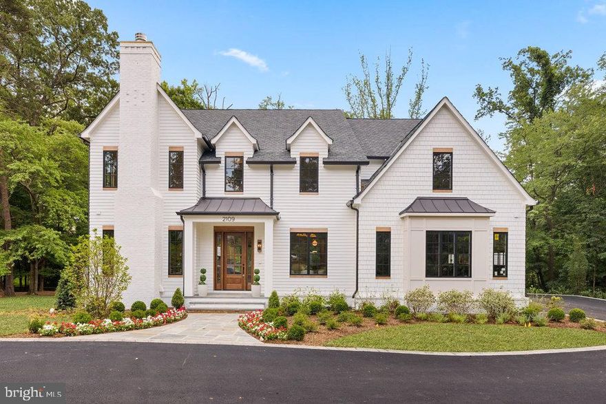 In the heart of Franklin Park, where wooded tranquility meets refined design, 2109 Elliott Avenue emerges as Brush Arbor’s newest expression of livable elegance—crafted in partnership with Wellhouse & Co. Set on a large, flat 0.57-acre lot at the end of a landscaped private lane and backing to protected green space, this sister property to 2107 Elliott offers a fresh perspective: more moody paint colors, and quietly bold with one additional bedroom and bathroom and a bonus pantry kitchen. 
Gabled rooflines, rich wood tone accents and dormer windows add architectural rhythm, while crisp landscaping elevates the curb appeal. The result is a home that feels classic yet current—elegant without excess, and perfectly suited to its tranquil, tree-lined setting, hinting at what lies inside: a layered interior of over 8,400 thoughtfully composed square feet, where smart design and dramatic contrast elevate every space.
Six bedroom suites, six full baths, three powder rooms, and three fireplaces are seamlessly integrated with dual staircases, a 3-car garage, and panoramic views into the lush, tree-framed rear yard. Throughout, custom cabinetry by Studio 37 and materials curated by Wellhouse & Co. deliver cohesion and character in every room.
Step inside to find herringbone white oak flooring in the foyer, brick floors in the family mudroom, and minimalist palette with ecru-trimmed white walls. The central family room is anchored by exposed beams and a statement fireplace, flowing effortlessly to a designer kitchen that balances warmth and polish. White oak cabinetry pairs with brushed brass fixtures, while the adjoining back kitchen—outfitted with its own refrigerator, microwave, and prep sink also offers sweeping views of the backyard and a discreet, elevated level of function.The covered porch with fireplace creates a true indoor-outdoor living moment. Special attention was given to the main level library, anchored by moody built-ins, the room features a rose-hued stone surround—cut in clean, modern lines for added depth and distinction.
A built-in desk in the upper foyer invites quiet focus, with oversized windows forming a natural backdrop. The primary suite is a sanctuary, with a spa bath drenched in light, and serene forest views from both the bedroom and the freestanding tub, as well as an expansive pair of adjacent closet suites—more akin to full-sized rooms than to closets.
In the lower-level, a flexible space has been thoughtfully designed for a future golf simulator, with swing-height ceilings and room to customize. Elevator-ready with dedicated shaft already constructed, the home is as practical as it is luxurious. The expansive, flat backyard is primed for a pool, sport court, or garden oasis—offering flexibility now and inspiration for the future.