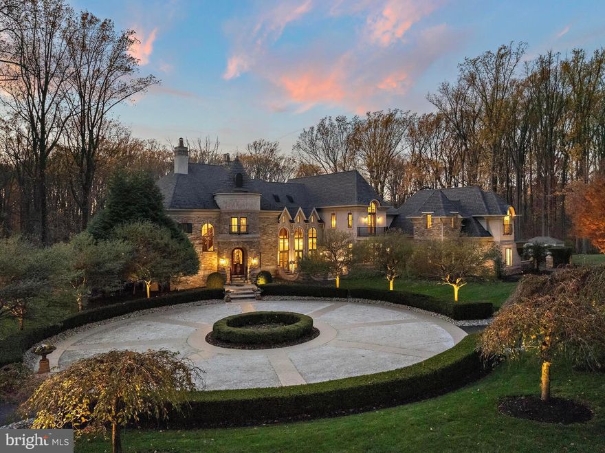 This stunning custom-built French Normandy estate is set on 5 private acres, backing to over 800 acres of preserved land within the Pennypack Trust. Originally designed as the personal residence of a renowned luxury builder, the home exemplifies exceptional craftsmanship, remarkable efficiency and extremely low property taxes. Secluded yet convenient, the property is just minutes from I-95 and the PA Turnpike, and only 5 minutes from shopping, dining, and everyday conveniences—offering the perfect balance of privacy and accessibility. The grand foyer features limestone floors, a coffered ceiling, and a double-sided gas fireplace shared with the formal dining room. The formal living room includes its own fireplace and French doors opening to a terrace ideal for elegant gatherings. The gourmet kitchen is a chef’s dream, with custom cabinetry, Calacatta marble countertops, hardwood floors, a spacious island, breakfast room with serene views, and a cozy hearth room with fireplace. Anchoring the main level, the two-story great room boasts a floor-to-ceiling stone fireplace and panoramic year-round views of the grounds. A private office and dual staircases complete this level.Upstairs, the luxurious primary suite features a sitting room, fireplace, multiple walk-in closets, a spa-inspired bath with double-headed shower, and private balcony overlooking the grounds. Three additional en-suite bedrooms and a conveniently located laundry room complete the upper floor. The finished lower level is perfect for entertaining, featuring a full bar, catering area, second kitchen, expansive seating and game spaces, a fifth bedroom with full bath, and a gym with glass walls offering stunning views that make you feel like you are exercising in nature. Outdoor living is exceptional, with expansive terraces overlooking peaceful, scenic grounds. A carriage house connected by a walkway with soaring 22' ceilings provides flexible space for an office, studio, or guest suite, with a three-car garage below—plus an attached four-car garage at the main residence.