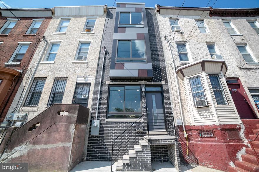 ​Built by Philadelphia Builder of the Year and quality production V2 Properties in 2019. This brick and contemporary metal panel three story structure touts a roof deck announcing extraordinary city views. Built in speakers for surround sound, a NEST thermostat, a hard wired alarm system, soft rounded wall corners, ambient lighting, trey ceilings, and always exquisite fixtures. An open floor plan concept entrance introduces the expansive living and dining rooms which open onto the spacious kitchen area. Grey toned wood flooring throughout. The kitchen features soft-close cabinetry, stainless steel appliances, and a center island with space for stool seating. Granite counters and attractive tile backsplashes add an elegant finishing touch. A generous patio sits off the back, bordered with an area for planting and fence. Contemporary metal banisters lead the way to the upper levels. The second floor holds two substantial bedrooms, on opposite sides of the house, each boasting high ceilings, recessed lighting, remote controlled ceiling fans, and large closets. The laundry room is conveniently placed on this level as well. A full bath boasts a shower with handsome tile surround, a vanity and mirror with industrial chic lighting. The master suite level is truly magnificent. A stately bedroom sits to the front of the house, crowned by stunning trey ceilings harboring soft ambient lighting and a remote controlled ceiling fan. A hallway, also adorned with trey ceilings and soft lighting, leads to not one but TWO walk in closets. The exquisite master bath stretches along the back, featuring an attractive double sink vanity accented with an elegant stone counter, two framed mirrors and unique lighting. A wide barn-door sliding glass shower encases a soft colored tile surround. A wine fridge and sink sit on the landing leading to the roof deck--a convenient perk for roof top entertaining. Here, nestled above the rooftops, you can relax to the music piped through the built-in speakers, and enjoy the city views, a comfortable respite from the urban fanfare below. The finished basement offers an additional bonus room with a full bath and closets for extra storage. This house checks all the boxes!