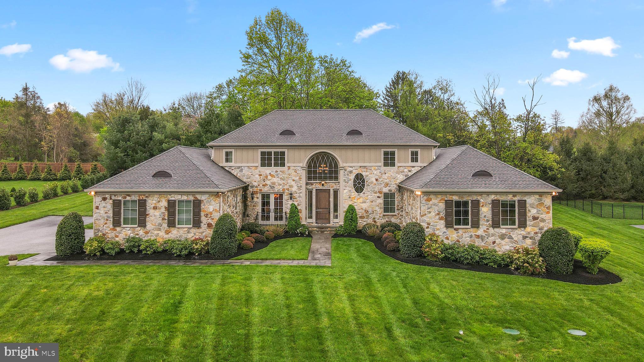 An expanded drive approach guides you to this stunning 4,854 sq ft stone manor set on a 1.2 acre in Worthington Green. The welcoming 2-story foyer provides a view with elegant interiors showcasing an open concept design with an architectural presence, a study showing wrap-around wood cabinetry, a formal dining room accented by wainscoting and French doors, and a defining family room adorned with a coffered ceiling, a cozy gas fireplace, and double French doors stepping to a patio. A coffered ceiling immediately grabs your attention in the family room hosting an ambient fireplace and double French doors lining the perimeter allowing for boundless natural light and access to a slate patio with stone retaining and sitting walls.
Equipped with professional upgrades, this chef's kitchen features a custom range hood and stainless steel appliances including a 5-burner gas cooktop, granite counters, basket weave tile backsplash, modern white cabinetry, hardwood flooring, a large island with a breakfast bar and sink, chic pendant lighting, and a spacious breakfast area ideal for casual dining. Main level owner's suite is highlighted by a sitting room, 2 large walk-in closets, and a double spa inspired bath with dual commodes, separate vanities, an oversized frameless glass shower, and a relaxing bubble tub. Upper level hosts 3 ensuite bedrooms, each with their own custom walk-in closet and just the right amount of natural light. Your chance to be creative and design the room of your dreams in the unfinished lower level, currently used as recreational space, which includes a walkout, insulated walls, a bath rough-in, and plenty of storage. This home is wired for a generator and has Sonos surround sound throughout the house. Desirable location just minutes away from fine dining, shopping, entertainment, schools, golf courses and country clubs, commuter routes, downtown Baltimore, and more!