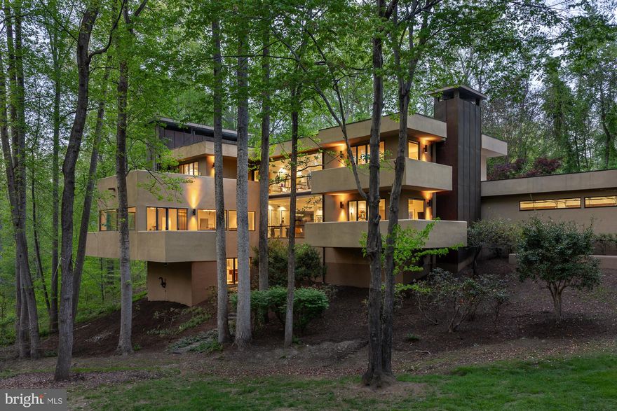 A two story gallery wrapped around an indoor koi pond forms the center of this quietly remarkable residence, where water, light, and movement shape the experience of the home from within.

Concealed within more than eight wooded acres, the approach unfolds gradually through dense trees before the architecture reveals itself, defined by strong horizontal lines, cantilevered forms, and a natural material palette that sits comfortably within the landscape.

Inside, the plan balances openness with clarity, offering a rare combination of architectural intent and everyday livability. Formal living and dining rooms, expansive gathering spaces, a dedicated office, and a well appointed kitchen with adjoining breakfast area are arranged with purpose and ease.

The upper level includes four generous en suite bedrooms, including a guest suite with a striking elevated terrace positioned within the treetops.

Constructed with steel framing and expansive structural glass, the home reflects a level of engineering integrity that supports its architectural ambition. Designed and built by local builder and engineer Jack Wilmore, whose background is rooted in generations of residential design and construction, the house carries a clear sense of authorship and discipline throughout.

Additional features include a three car garage, multiple outdoor terraces, and a setting that offers both privacy and proximity to the Washington metropolitan area.

A distinctive offering for those who value architecture that is considered, enduring, and deeply livable.

A detailed video is available by searching the property address.