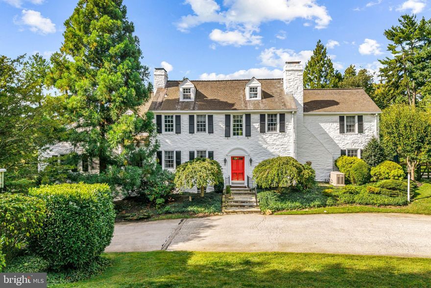 Surrounded by pastoral beauty and across from preserved land, this classic 1930s Main Line estate blends privacy with convenience in one of Gladwyne’s most desirable settings. The painted white stone exterior with black shutters captures timeless character on 2.47 acres with sweeping lawn and mature landscaping. 1324 Youngsford Road encompasses a main residence with 7,112 square feet on three levels—five bedrooms, five full and one half bath—along with a two-bedroom, two-bath carriage home. Combined home and carriage house offers 7 beds, 7.5 baths,
The main level showcases  distinguished spaces, where old-world character meets architectural detail. A slate walkway with wrought-iron railing leads to the front entry, opening to a foyer that introduces gracious gathering rooms. Straight ahead, the dining room is framed by a wide triple window, creating a beautiful setting for formal dining. To the right, the living room impresses with wide-plank hardwood floors, soaring ceilings, and a paneled fireplace surround that reflects the home’s craftsmanship. French doors open to a side slate terrace with a stone sitting wall overlooking the pool and gardens, while expansive windows and doors throughout this level flood the rooms with natural light. From the living room, two openings connect to the striking family room addition by renowned builder E.B. Mahoney. Distinguished by generous proportions, hardwood floors, and a wall of windows, this light-filled space is the heart of the home. A second fireplace adds warmth, while French doors extend the living space outdoors. A hall off this room houses a three-stop elevator serving the lower level and primary suite. A cozy sitting room with built-ins and the home’s third fireplace provides an intimate retreat, while a powder room is conveniently placed off the foyer. The sunny kitchen offers three windows, a side door, and an adjoining breakfast nook with a bay window for casual meals. This wing also includes an office, laundry room, full bath, and rear staircase. While functional, these spaces offer opportunities for customization or a more open layout.
Upstairs, the expansive primary suite spans an entire wing with a spacious bedroom, walk-in closets with built-ins, and a sitting room that can serve as a home office or quiet retreat. The en-suite bath includes a large vanity and water closet, with space for updating. Bedrooms two and three share a Jack-and-Jill bath, while bedroom four enjoys its own en-suite bath and walk-in closet. The third floor features a fifth bedroom with en-suite bath—ideal for a guest or Au pair suite. All bedrooms are carpeted, with hardwood flooring underneath awaiting refinishing.
The walk-out lower level offers a recreation room with slate floors, panelled walls, beamed ceilings, a bar, and the home’s fourth fireplace. French doors open to a slate patio and the rear yard, providing access to the pool and gardens for entertaining. Storage areas, utilities, and interior access to the side-entry two-car garage complete this level.
A separate carriage house provides 1,581 square feet of flexible space with living, dining, kitchen, bedroom, and full bath on the main level, plus a second bedroom and bath upstairs. Ready for cosmetic updates, it offers versatility for guests, in-laws, or business use, supported by the property’s license. Outdoor amenities include a pool with patio and greenery, a stone pool house, and expansive lawns with mature landscaping that create a picturesque setting.
With timeless architecture, distinguished spaces, and strong bones to be re-imagined, this is a rare opportunity to own a standout home in one of Gladwyne’s most coveted settings. Just half a mile from the Village of Gladwyne and close to Kenealy Nature Park, the Bridlewild Trail, and award-winning Lower Merion schools, the property offers both tranquillity and accessibility. Narberth Station is three miles away with service to Philadelphia and New York.