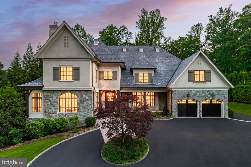 Graciously tucked away at the end of a verdant street in Bethesda’s prestigious Bradley Hills Grove, 6910 Blaisdell Road is a stately stone and stucco chateau that masterfully blends timeless architecture with bespoke craftsmanship. Designed and constructed by, and for, esteemed custom builder Richard Cantor, the residence spans over 12,500 square feet of exquisitely finished living space—a rare fusion of grand scale and thoughtful detail.
 
A sweeping circular drive welcomes guests, while the commanding façade—stone and stucco topped by a slate roof—establishes an immediate sense of presence and permanence. Inside, Versailles-patterned travertine floors and a dramatic curved staircase anchor the grand foyer, setting the tone for the refined interiors beyond. Solid cherry hardwoods, intricate millwork, thick moldings, and soaring ceilings underscore the home's elevated quality.
 
Gracious formal rooms unfold from the reception area. The living room shares a double-sided fireplace with an intimate sunroom, while the 24-foot-deep dining room is anchored by its own roaring fireplace and rustic beamed ceiling. French doors reveal a dignified library lined with sturdy built-ins and served by a nearby wet bar—an ideal setting for quiet work or entertaining.
A diagonal coffered ceiling adds architectural drama to the informal living areas. At the center is a sprawling chef’s kitchen, where furniture-grade cabinetry pairs beautifully with professional-grade Wolf and Sub-Zero appliances. The adjoining breakfast room, wrapped in curved windows, overlooks the rear terrace and wooded views beyond, sharing a double-sided fireplace with the outdoor space.
 
The family room features a floor-to-ceiling limestone fireplace, wood-beamed ceiling, and triple sets of French doors opening onto an expansive flagstone terrace. Shaded by mature foliage and fully equipped with an outdoor kitchen, it’s a dream setting for al fresco dining and entertaining. A true butler’s pantry, generous mudroom with a second powder room, and access to the four-car garage with EV charging complete the main level.
 
Upstairs, the lavish primary suite occupies its own private wing. Separate sitting and sleeping areas evoke the feel of a luxury hotel suite, while a private balcony offers tranquil treetop views. Two large walk-in closets and a third, bedroom-sized dressing room with a center island provide abundant storage. The travertine-clad primary bath features dual vanities, a makeup counter, walk-in steam shower, and a jetted infinity tub.
 
Three additional ensuite bedrooms include a luxurious princess suite with its own sitting room. A shared family lounge and a well-appointed laundry room add function and flexibility. The top level offers nearly self-contained living quarters, with a large flexible space and full bedroom suite—perfect for a home office, yoga studio, or guest apartment.
On the lower level, the home reveals its true entertainer’s heart. A temperature-controlled 1,000-bottle wine cellar, accessed via wrought iron door, serves a central wet bar. The fitness center includes its own spa bath with sauna and steam shower, while the professionally outfitted home cinema boasts immersive 5.2 surround sound. A walkout recreation room, game room, additional bedroom suite, and ample storage complete the lower level.
 
Technology is seamlessly integrated throughout. A dedicated AV room houses a Leviton full-home computer-controlled lighting system, comprehensive security and fire suite with video surveillance and audio alerts, and a full-house generator for peace of mind.
 
Moments from Burning Tree Country Club, top-rated schools, and major commuter routes, 6910 Blaisdell Road presents a rare opportunity to own a legacy estate in one of Bethesda’s most coveted enclaves.