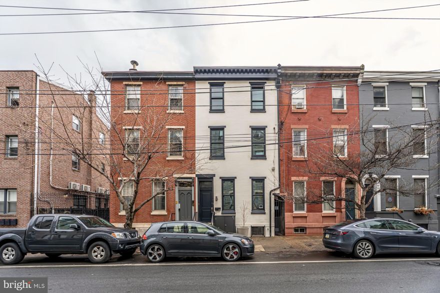 Set in the sought after neighborhood of Northern Liberties, this Victorian blends historic character with a thoughtful, modern renovation. The entry vestibule sets the tone right away—original wood detailing, a transom window, and a sense that the home’s history has been carefully preserved, not replaced. Inside, the main living space feels both open and grounded. Oversized windows bring in natural light, while a fireplace and statement chandelier anchor the room, creating an easy rhythm for everyday living and entertaining. The kitchen is designed to be lived in. LG smart appliances, a six-burner double oven, pot filler, and black quartz countertops pair with abundant cabinetry and a large island with seating. Just beyond, a light-filled dining area and convenient pantry add both function and flow. A powder room is tucked discreetly nearby. Out back, a private yard extends the living space outdoors, with stone pavers, a cedar privacy fence, and a custom self-watering planter system. A reclaimed firepit creates a natural gathering point. The second level is centered around the primary suite. The bedroom is spacious and calm, with a dedicated, detached walk-in closet room and a spa-like bath featuring a soaking tub, oversized walk-in shower with dual shower heads, and refined finishes throughout. This floor also includes a second bedroom and a fully outfitted laundry room with LG appliances, a utility sink, built-in clothing steamer, and generous storage. A half level up, a flexible bonus space functions as its own private suite, complete with a full bath and kitchenette—ideal for guests, extended family, or a separate entertaining / living area. The third floor offers two additional bedrooms, each with great light and closet space, along with extra hallway storage. Downstairs, a large basement with high ceilings provides excellent storage and future potential. Additional details include keyless entry, dual-zone climate control with digital thermostats, and upgraded bathroom features like heated seats and bidets on all toilets. The seller currently holds two parking licenses for the PPA-owned lot at 982 N 6th Street (Inquire for details).  Located in the heart of Northern Liberties, you’re just a short walk to the award winning Little City Montessori as well as Liberty Lands Park, Cruz Park, and The Piazza. You'll be surrounded by some of the neighborhood’s most loved spots...Weeknight dinner at North Third, cocktails at Standard Tap, or a casual night at Jerry’s Bar. Brunch at Café La Maude or Honeys Sit and Eat, or coffee at One Shot Café and Menagerie. It’s the kind of neighborhood where your regular spots become part of your routine.