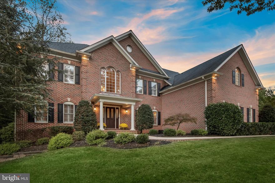 Stunning brick-front estate in Pindell Woods, one of Fulton’s most sought-after communities, set on nearly an acre at a premium corner homesite. Offering over 6,000 square feet across three finished levels, this residence is complemented by a private, retreat-style backyard designed for exceptional outdoor living, featuring an expansive patio and a rustic stone outdoor fireplace. Notable upgrades include a new A/C system, fencing, carpeting throughout, washer and dryer, as well as a whole-home water filtration system.  A sun-filled two-story foyer welcomes you with hardwood flooring and a grand staircase adorned with black iron balusters, framed by wide arched openings to the formal living and dining rooms enhanced with elegant accent molding. The impressive two-story great room showcases a dramatic floor-to-ceiling rustic stone fireplace with an upper overlook and flows seamlessly into the gourmet kitchen. Here, an oversized tiered island, granite countertops, tile backsplash, rich wood cabinetry, and stainless steel appliances, including wall ovens and a beverage cooler, create the perfect setting for entertaining. Glass French doors lead to a private home office, while a spacious laundry room and powder room complete the main level.  Upstairs, the luxurious primary suite offers a tranquil sitting room, dual walk-in closets, and a spa-inspired bath with dual vanities, a soaking tub, and a frameless shower with seating, rainfall, and handheld shower heads. A second bedroom features its own en suite bath, while two additional bedrooms share a third bathroom.  The finished lower level is designed for leisure and lifestyle, featuring a recreation room with a stone fireplace, a four-person wet bar, a dedicated exercise area with mirrors, rubber flooring, and custom lighting.  Step outside to the fully fenced backyard oasis, where an expansive bluestone patio, outdoor fireplace, open play areas, and a serene wooded backdrop provide the ultimate setting for relaxation and gatherings.  Ideally located between Maple Lawn, Columbia, and Clarksville, this exceptional home offers convenient access to abundant shopping, dining, entertainment, and major commuter routes.