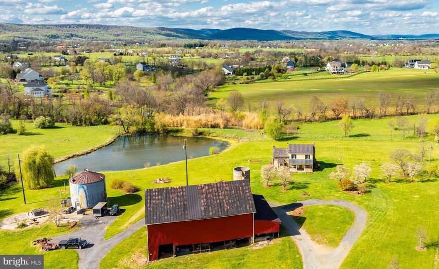 Welcome to 38620 Patent House Lane—a rare opportunity to own a beautifully maintained 2 bedroom, 2 bath farmhouse nestled on a stunning 20-acre conservancy. From its expansive outbuildings to its peaceful pear orchard, this property offers the perfect blend of rustic elegance and modern comfort.

Step inside to a spacious living area featuring exposed logs and beams, custom built-ins, hardwood flooring, and two cozy fireplaces—ideal for curling up with a book or enjoying casual gatherings. The stone addition includes a formal dining room with exposed stone walls, a striking stone fireplace, and an antique built-in china cabinet—perfect for intimate entertaining and memorable dinners.

The beautifully upgraded eat-in kitchen boasts stainless steel KitchenAid appliances, custom wooden cabinetry, a farmhouse sink, and stunning tile work, making it a dream for both cooking and entertaining. Convenient main-level laundry adds to the home's functionality.

Upstairs, you'll find two spacious bedrooms with charming built-ins and rich wooden detailing, creating a warm and timeless atmosphere. The updated full bath features a sliding barn door and subway-tiled shower for a touch of modern flair.

Outside, three porches and a large deck overlook the breathtaking 20-acre property, complete with a tranquil pond, a three-season office, a substantial barn and an improved silo that offers additional usable space—perfect for storage, creative pursuits, or future customization.

Located just minutes from downtown Lovettsville, as well as local breweries, vineyards, shopping, and all that Northern Virginia has to offer, this is a rare opportunity to own a serene countryside retreat with modern comforts and timeless charm.

Enjoy, and welcome home!