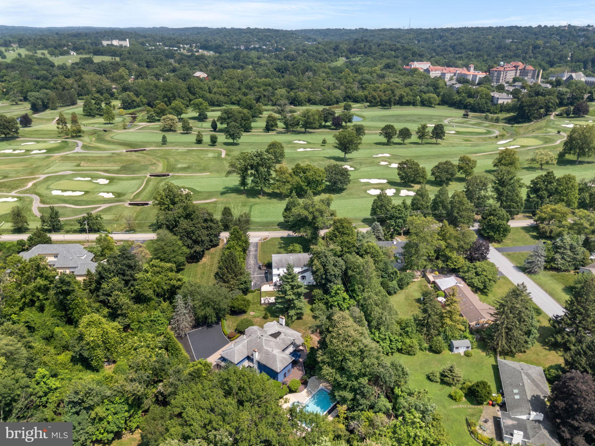Tucked at the end of a long private driveway and set across from the Whitemarsh Valley Country Club, this well-appointed residence offers an exceptional combination of privacy, comfort, and convenience. Upon entering through the center hall you are immediately struck by the potential in this unique and inviting floor plan with its marble floors, vaulted ceilings, exposed beams, and abundant natural light. To the left, the formal living room features plantation shutters and a marble-surround gas fireplace. Step down to the dining room, which boasts the same high ceilings and direct access to the expansive rear deck—ideal for alfresco dining and entertaining.The well-designed kitchen is equipped with stainless steel Thermador appliances, including a five-burner built-in range, wall-mounted oven with warming drawer, and a double refrigerator/freezer. The oversized island with Brazilian Quartzite counters offers bar seating and a distinctive modern sink. The kitchen flows seamlessly into the sunken family room, which features a built-in sound system, gas fireplace, and custom built-ins. At the rear of the home, a full bathroom and dressing room provide direct access to the pool and backyard for added convenience. This level is completed by a guest bedroom with an en suite bath, a laundry room, and a three-car garage.
Upstairs, French doors open to the primary suite, highlighted by vaulted ceilings, a gas fireplace, and an abundance of walk-in closet space. A private study with floor-to-ceiling bookshelves and a rolling library ladder provides a comfortable home office or reading retreat. The primary bathroom includes a double vanity, jetted soaking tub, and a walk-in shower. The second suite offers a spacious bedroom, walk-in closet, and en suite bathroom. Two additional guest bedrooms and a full hall bath complete this level.
The finished basement is ideal for entertaining, offering high ceilings, a projector with built-in sound system, and a wet bar equipped with a beverage refrigerator and ice maker. Additional spaces include a home gym with rubber flooring, ample storage closets, and a half bath.
Outside, the large wooden deck wraps around the back of the home, offering multiple spaces for dining, lounging, and relaxation. Just steps away, the heated pool and spa—with built-in automatic cover—provide an inviting setting for summer enjoyment. A playground and asphalt sports court with basketball hoop add to the property’s versatility. Set on 1.28 acres and fully fenced, the landscaped grounds are surrounded by mature trees for privacy. The home is conveniently located just minutes from Morris Arboretum, Koontz Park, and the shopping and dining of both Chestnut Hill and Wyndmoor—offering a peaceful setting with excellent access to the area’s amenities.