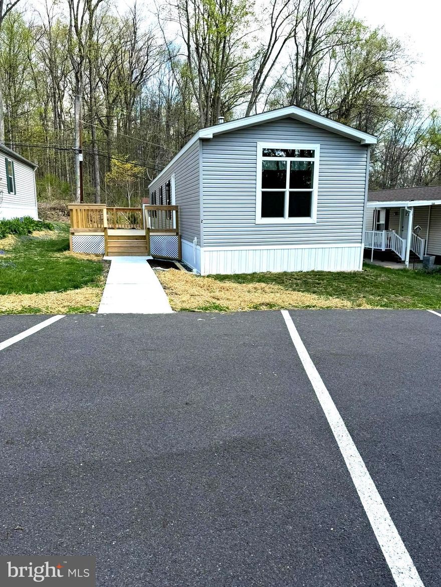 Nestled in a peaceful country setting yet conveniently close to everyday amenities, this brand‑new Pine Grove manufactured home offers exceptional comfort, quality construction, and low‑maintenance living in a well‑kept 55+ community with a low $500 monthly fee that includes water, sewer, and trash. Built on concrete piers set on a concrete slab and constructed with 2x6 exterior walls, this home features recessed lighting, a full drapery package, and a beautifully designed large kitchen with a center island, abundant counter space, and extensive 42" wall cabinets. The thoughtful floor plan places the two bedrooms at opposite ends of the home, providing added privacy for guests or flexible living arrangements. There are 2 full bathrooms, including a main bath with a 60" fiberglass stall shower featuring dual seats and a door. Enjoy the outdoors on the new 12' x 20' deck with two sets of steps, a concrete walkway, and full skirting around the home. A dedicated laundry room with washer/dryer hookups and outside access adds convenience. Additional highlights include two owned propane tanks, stainless steel appliances (self‑cleaning gas range, dishwasher, and refrigerator with ice maker), propane heat and cooking, two assigned parking spaces plus nearby guest parking, and an 8' x 12' shed with ramp for easy storage. Situated in a desirable location within the park with scenic country views, this home blends tranquility, modern comfort, and accessibility in a beautifully maintained community.