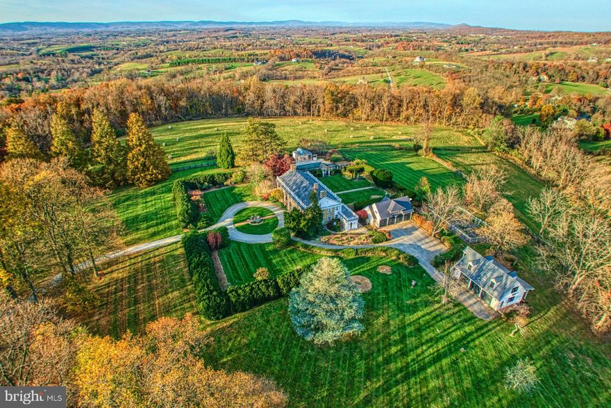 Perched superbly on a rise, Burr Ridge offers breathtaking panoramic views that span three states with iconic Sugar Loaf Mountain gracing the horizon.  The 1936 5-bedroom stone home stands as a timeless testament to architectural elegance and historical charm.    Approaching the home along the winding drive that is graced with lush landscaping and mature trees you're immediately struck by its classic beauty and stately presence.   
As you step inside, you are greeted by the timeless charm of wood floors, high ceilings and a curved staircase that serves as a focal point inviting you to explore further.  The living spaces are spacious and inviting with an abundance of natural light.  
The outdoor spaces are perfect for relaxing or entertaining with plenty of room for outdoor dining in the summer kitchen or lounging at the stone patios. The grounds are beautifully landscaped with a pool, pool house, formal gardens and fenced kitchen garden space.  
Accessed by paved roads, the property also features two detached garages with parking for up to seven cars ensuring ample space for vehicles and storage.  Additionally, a one-bedroom apartment offers flexibility and convenience, ideal for staff or as a private retreat.  
Nestled on over 50 acres of rolling land, this farm  is located minutes from downtown Leesburg and the Toll Road.  Not in a conservation easement this property provides flexibility for future use and development.  Currently the farm itself is a working property with acres of open fields and pastureland used for cattle and complemented with acres of hardwoods. 
In addition to the main house, the property boasts a three-bedroom guest house, providing comfortable accommodation for visitors or additional living space.  This separate dwelling offers privacy, convenience and its own address making it ideal for hosting guests or as a rental opportunity.  
In every detail Burr Ridge exudes a sense of warmth with its perfect blend of natural beauty and rural charm.  This is truly a unique opportunity to experience the best of Loudoun County country living!