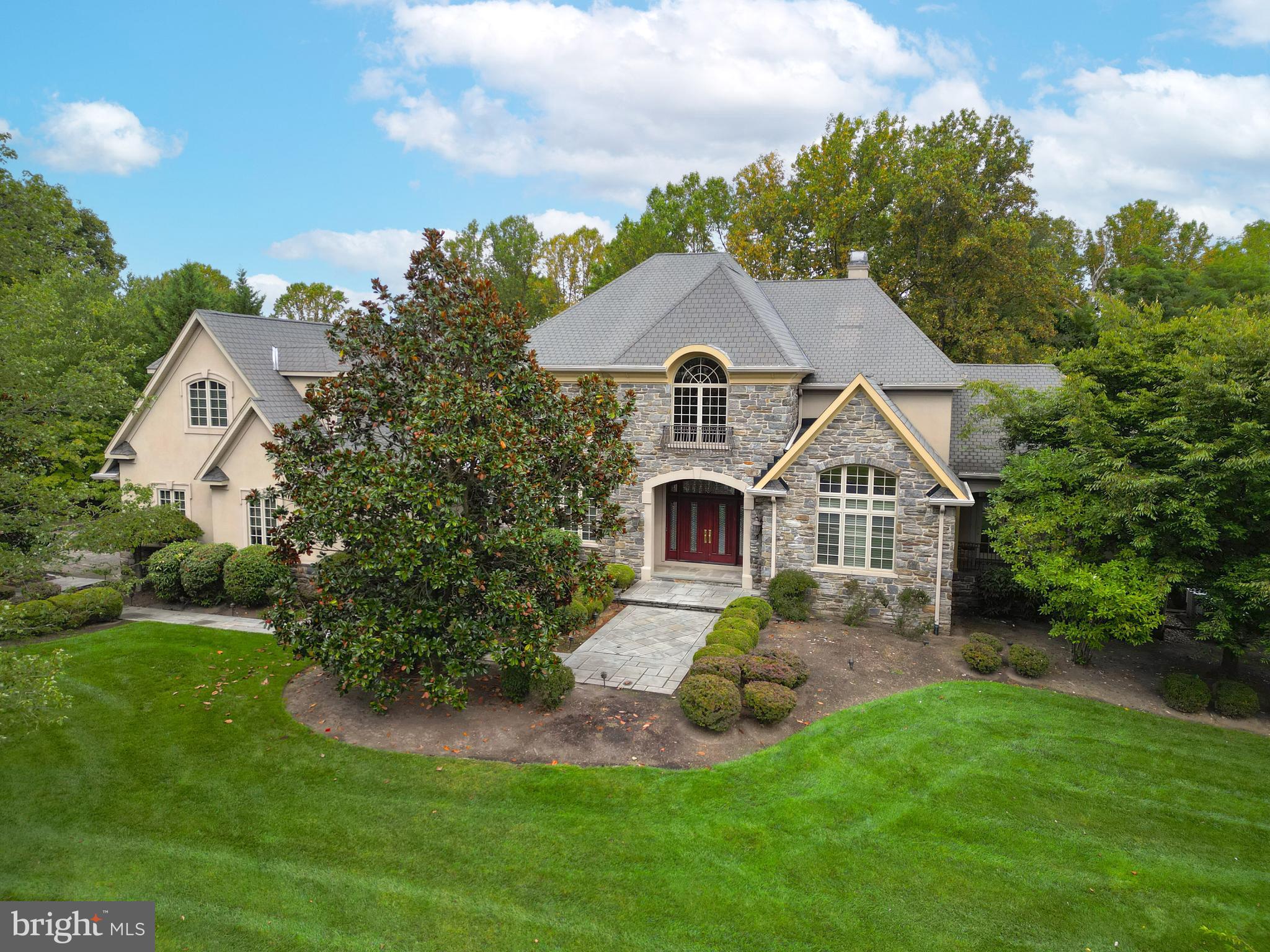 Truly a dream home in prestigious Inverness! An exceptional opportunity to own a masterpiece of timeless elegance and modern sophistication. Nestled in one of the most coveted enclaves, this stunning property is set on beautifully landscaped, wooded grounds offering both privacy and natural beauty. From the moment you approach, the stately stone façade and elegant architecture set the tone. A meticulous stone walkway leads to custom wood double doors, opening into a grand entry hall with exquisite marble floors and a dramatic curved staircase—an architectural work of art. Soaring ceilings, custom millwork, and expansive windows create an atmosphere of refined luxury throughout. The main level boasts custom recessed lighting and imported chandeliers. The formal living and dining rooms are expertly appointed with extensive built-ins, while the family room features a gas fireplace, built-in wall unit, tray ceiling, and a striking window wall with French doors opening to the remarkable grounds. A chef’s dream, the gourmet kitchen is equipped with exotic hardwood cabinetry, premium Miele appliances, a Sub-Zero refrigerator, two dishwashers, two ovens, and a large Butler's pantry. A sun-filled breakfast area with a window wall provides tranquil views of the private backyard and leads to a spectacular multi-level bluestone patio—perfect for entertaining. The primary suite is an elegant retreat, featuring a tray ceiling, gas fireplace, sitting room with private patio access, and an expansive custom walk-in closet. The luxurious primary bath includes a dressing area, soaking tub, and walk-in shower—all framed by serene views. Also on the main level: a powder room, spacious laundry room, and mudroom. Upstairs, gleaming hardwood floors and an open sitting area with built-ins welcome you. French doors open to a private office, while four generously sized bedrooms and three full baths offer comfort and space for family or guests. A large recreation/family room could easily serve as an additional bedroom or work space. A second laundry room with abundant cabinetry completes the upper level. The walk-out basement presents endless possibilities—already roughed in for two bathrooms or a wet bar, ready to be customized to your needs. Car enthusiasts will love the beautifully finished, heated 4-car garage with a professional lift to accommodate a fifth vehicle. Additional features include a ¾ house generator, extensive hard-wired security system, Pella windows with built-in slim shades, and countless custom upgrades. Located in the highly sought-after Lower Moreland School District, with convenient access to major roads, parks, restaurants and shopping. This is more than a home—it's a lifestyle. A must-see property offering unmatched craftsmanship, comfort, and luxury.