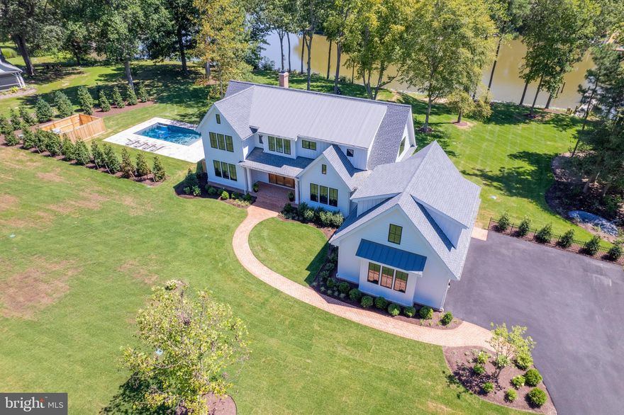 After turning off St. Michaels Road, you soon leave the traffic noise behind as you drive past deep farm fields on Leehaven Road. The landscape then turns into a wooded area with houses along this dead-end road that is surrounded by Dixon Creek that leads to the Tred Avon River. The lot is wide and deep with the house set back far from the road. Mature evergreens have strategically been planted to provide privacy from adjoining neighbors. The house and pool footprints are parallel to the shoreline to provide maximum water views from the main rooms and for relaxing after a dip in the large pool. This “custom” build is one of a kind in today’s market. The architectural style of this home is the popular Farmhouse Chic white Hardie Plank siding with contemporary accents of sleek black window frames, white trim and gray metal roof.
The mahogany front double doors with full sidelights open into the foyer with a wide “U” shaped stair to the second floor. You are immediately drawn to the vista through the living room windows to views of the water and the living room is open to both the kitchen and the dining area that feels like a sunroom with its wrap-around windows. The covered porch with access from the living room and main floor primary suite extends your waterside living space. Off the kitchen are the service areas of laundry, mud room and the side-facing large two-car garage with stairs to a bonus room above. The second floor contains a sitting area, another primary suite and two other en-suites. 
This turn-key, quality built home was built by Focus Construction to the highest level of detail including spray foam insulation throughout, conditioned 5’ crawl space, and heated bathroom floors. Amenities include wood floors throughout the house, wood burning fireplace w/ gas hookup in the living room, central vac, security system including camera hookups. Professionally landscaped property including full irrigation, new living shoreline, and new pier with water and electric. If you are seeking a “plug and play” waterfront property, look no further than the serenity of Leehaven!  2 miles from downtown Easton!  Great internet and cable!  Installed propane powered generator! This property comes with a 1 year bulder warranty!  Builder matterport available. Not in Flood Zone! Property is shown by appointment only.