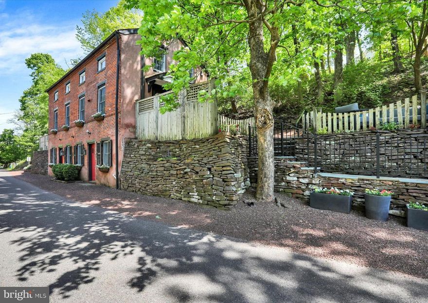 The Circa 1780’s “Bank House” located in the heart of New Hope Borough is a classic late 1700’s Bucks County home, benefiting from extensive renovations while preserving its historic and pristine character. Some of the many original features include 14”+ wide plank pumpkin pine flooring, multiple sets of pie staircases, and original doors and hardware.  This red brick home is situated on a quiet country road, affording privacy plus scenic views of the Aquetong Creek from its hilltop setting. The home has 3 dedicated on-street parking spots and is a 5-minute walk to the wonderful heart of New Hope and the Delaware River. Bluestone stairs with classic cast iron railing and stacked-stone walls lead to the Main level kitchen patio area and the kitchen entrance of this historic treasure. The gourmet kitchen boasts original pumpkin pine flooring, recessed lighting, white full overlay custom cabinetry with solid wood countertop, and a two-tier Bucks County Soapstone island with soapstone sink, counter and breakfast bar. Also featured are high-end stainless-steel appliances including a “Jenn Aire” French door refrigerator, a Miele dishwasher, an Italian F. Bertazzoni dual-fuel range with red enamel finish and a stainless-steel F. Bertazzoni microwave oven. There is also a spacious dining area with a wall of windows. Dual sets of original pie stairs with original doors lead to the Upper and Lower levels. A small hallway with both coat  & storage closets ushers you into the living room. The living room features original flooring, a fireplace with a gas fired cast iron gas stove insert,  custom-built corner cabinetry and recessed lighting. The sun/garden room provides an area of tranquility and features dual walls of windows, pine wide plank flooring, a mini split HVAC unit for zoned heating/cooling, a cathedral ceiling and sliding door access to a newly built brick patio, one of several outdoor areas. A powder room is conveniently located in the sun/garden room area. Take the living room pie staircase to the Lower level to the spacious owner’s suite which features pine flooring with radiant heat, a dry stacked stone fireplace with wood mantle, a closet, and recessed lighting. The remodeled owner’s bath includes 12” slate tile with radiant-floor heat, a tiled walk-in shower with a frameless glass enclosure & repurposed antique Vanity. From the bath, a spacious hallway has utility and storage closets leading to the voluminous laundry room with painted wood plank floors, recessed lighting, storage cabinetry, a vintage wash tub and one of two 1700’s original entrance doors to the street level. The Upper level features three additional bedrooms and two full baths!  Bedroom #2 includes original flooring, an angled ceiling, a custom-built wardrobe, and the original door/hardware. Bedroom #3 includes original flooring, a vaulted ceiling with skylight, a zoned mini-split HVAC unit, a built-in closet, tongue & groove slat wainscot and the original door/hardware. Bedroom #4 includes original flooring, dual skylights, exposed beams, a zoned mini-split HVAC unit, a large dressing/open closet area with hanging space and shelf storage. Adjacent to Bedrooms 2 and 3 is a full bath #2 featuring a walk-in shower, marble basketweave tile flooring, a skylight and linen closet. Adjacent to Bedroom 4 is bath #3 featuring a corner tub/shower, marble basketweave tile flooring, a double vanity and linen closet. This beautiful home is located in New Hope Borough just a five minute walk to the much-loved restaurants including Carla’s, Nektar, Zoubi, and Nozomu. Enjoy plenty of dining, shopping, antiquing, and entertainment including the Bucks County Playhouse. Some outdoor activities these two river towns offer includes walkable access to both the 58-mile Delaware Canal Towpath in PA and the 32-mile Delaware & Raritan Canal Towpath in NJ. This location is commutable to New Jersey, New York, Philadelphia, and the Poconos.