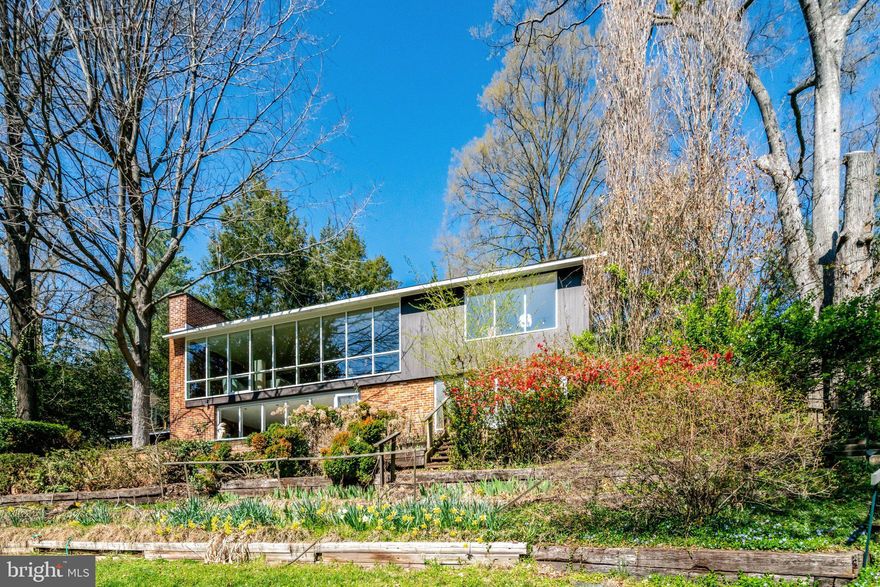 This two-level Goodman mid-century modern home offers more space and light than you might expect from the street. A private front patio creates a quiet entry, leading into a slate foyer with additional storage. As you step inside the living room, the home opens up dramatically, set high on the hill with walls of windows that frame wide, elevated views of nearly half an acre of yard. Natural light carries throughout the main level. The flexible layout includes 3 to 4 bedrooms. The fourth room is currently set up as a dining room or office and can easily function as a bedroom again. The kitchen is large, neutral, and ready for everyday use or future updates. The living room also features a wood-burning fireplace.

The lower level includes a spacious recreation room with another fireplace, more windows overlooking the back patio, and two additional bedrooms. One bedroom has two dramatic walls of glass. There is also a second European-style full bathroom with dual sinks, a bidet, and a walk-in shower. A separate storage room includes laundry, a utility sink, and ample storage space. Recent improvements include refinished hardwood floors on the upper level, new carpet downstairs, fresh paint, and double-pane windows throughout. The grounds offer a mix of paths, tiered landscaping, and a large grassy backyard. The setting feels private and connected to nature, with the kind of indoor-outdoor flow that is characteristic of Hollin Hills homes.