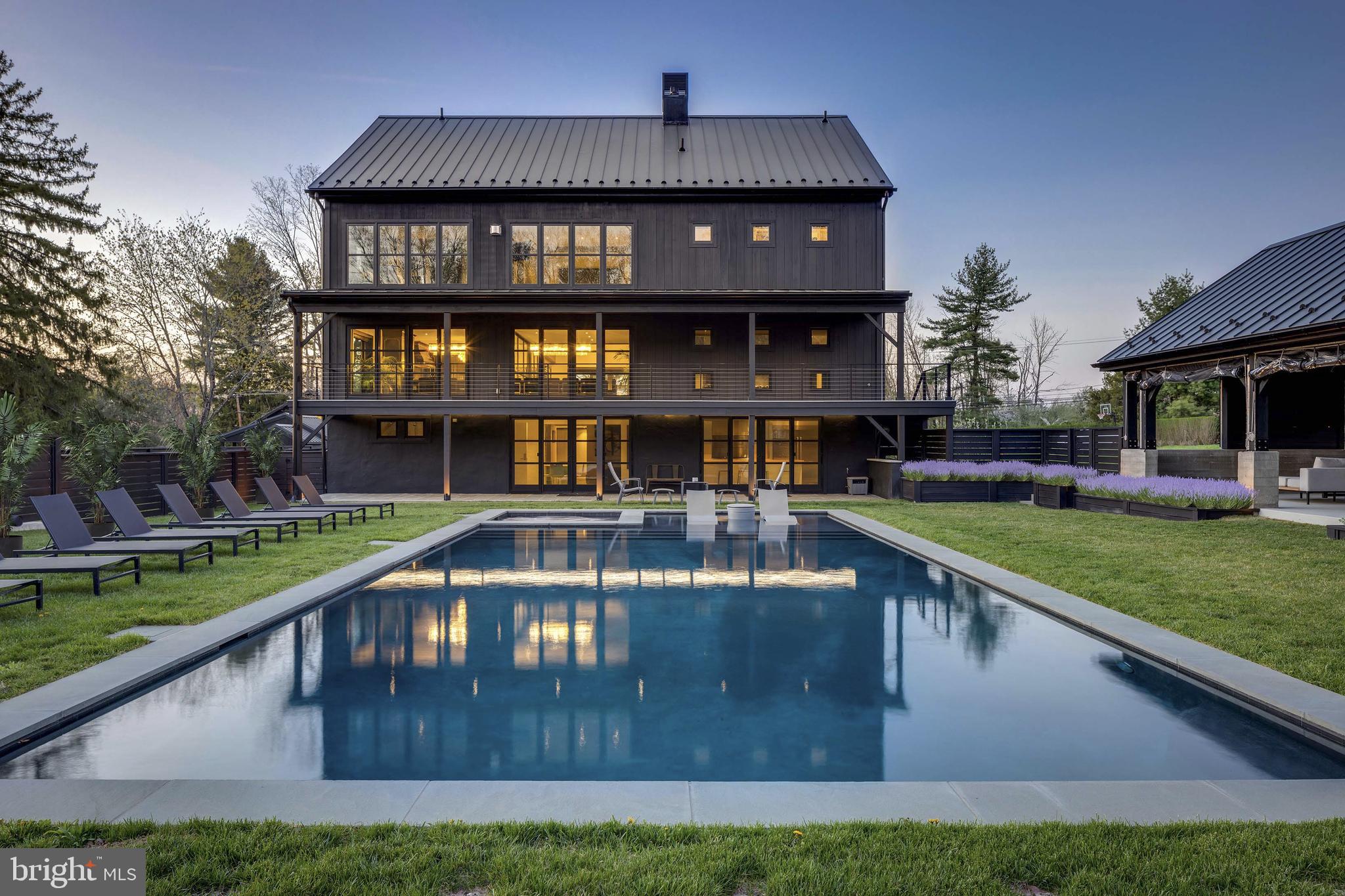 Welcome to a truly exceptional property where innovation, luxury, and sophistication come together. This magnificent estate, spanning over 10,000 square feet and nestled on a sprawling 10.5 acre lot, is a one of a kind home that offers both unparalleled comfort and cutting-edge design. Located in the heart of Bucks County, this residence blends modern living with forward-thinking technology, making it a standout in New Hope’s real estate landscape. Designed with purpose and built for luxury, the home spans four living levels serviced by an elevator and a stunning floating steel stair tower enclosed in glass. The expansive main living area is highlighted by an impressive bar featuring illuminated glass shelving set against smoked mirrors, flanked by two 450-bottle wine cellars, perfect for wine lovers and entertaining guests. The chef’s kitchen is a culinary masterpiece, complete with a custom-built La Canche range from Paris, Sub-Zero fridge and freezer, and Miele appliances offering versatility and precision. The cabinetry was designed specifically for the space by Plato, and the expansive island comfortably seats eight, making it a perfect spot for gatherings. With six spacious bedrooms, each featuring its own en-suite bathroom and custom closets, this home ensures both privacy and comfort for all. The top floor offers a tiered movie theater with a bar and gaming center, ideal for cinematic experiences and entertainment. The bottom floor features an additional chef’s kitchen, perfect for hosting gatherings. Outside, you’ll find a luxurious heated pool and spa, surrounded by imported palm trees, a Sonos sound system, and an outdoor shower for added convenience. In addition to the main residence, the property boasts three impressive outbuildings. The first is a remarkable 1,300-square-foot event PAVILION, heated with seasonal enclosures and furnished with contemporary pieces that create an elegant atmosphere. Inside, you’ll find a 22-seat bar with three TVs, a hanging fireplace imported from France, and a fully stocked outdoor chef’s kitchen. This kitchen includes a pizza oven, Japanese Hibachi tables, and a custom-built smoker designed and fabricated by Pastella | Burns, making it a dream for grilling enthusiasts. Adjacent to the home is a Hampton-inspired guest cottage, featuring a bedroom and full bathroom providing a private retreat for guests. The property also includes a spacious 1,500-square-foot bi-level CARRIAGE HOUSE, complete with a bedroom, full bathroom, state-of-the-art fitness center, dance studio, and an upstairs office with a full kitchen and bathroom that can be converted into a separate residence. These exceptional amenities provide the ultimate setting for relaxation, entertainment, and an elevated lifestyle.