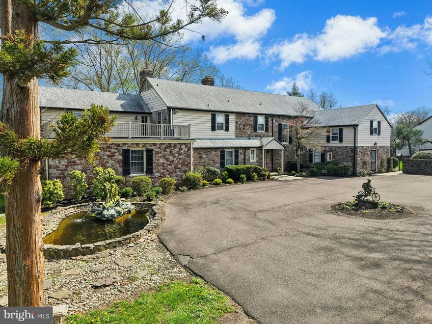 Presenting the historic Fashion Farms headquarters.  Set along the banks of Pidcock Creek in one of Buckingham Township’s most scenic and enduring agricultural corridors, this extraordinary 57-acre estate offers a rare convergence of land, legacy, and lifestyle. Framed by rolling hills and protected vistas, the property reflects a landscape shaped by generations of stewardship, where the natural beauty of Bucks County unfolds in every direction. At the center of the estate, a substantial stone residence of over 6,700 square feet embodies both grandeur and warmth, offering 6 bedrooms, 4 full and 2 half baths. Designed for both refined living and relaxed gathering, the home features grand living and dining rooms and a richly appointed trophy room/office—a distinctive nod to the legacy of Fashion Farms and its place within the harness racing world. The chef’s kitchen is anchored by an impressive 15-foot island and elevated appliances, while a sunroom with vaulted ceilings captures magnificent views of the surrounding countryside. A main-level bedroom suite connects to a private wellness retreat complete with gym, sauna, steam room, and access to an outdoor hot tub. The upper level presents a luxurious primary wing featuring a grand, generously scaled sitting room with an exposed fieldstone wall, creating a striking architectural focal point. The primary bedroom offers its own fireplace and is complemented by a dressing room and well-appointed bath, while a private staircase provides convenient access to the home’s wellness spaces. Additional bedrooms and baths provide comfort and flexibility. A climate-controlled wine cellar completes the lower level. A Pennsylvania bluestone patio extends the living space outdoors, inviting quiet enjoyment of the property’s remarkable setting.  Originally established as the headquarters of the renowned Fashion Farms breeding and racing operation, the property carries a legacy of purpose and excellence. The land itself, traversed by Pidcock Creek, is part of a historic corridor dating back to the earliest settlement of Bucks County. The farm is thoughtfully improved with extensive equestrian facilities, including a stallion barn with heated lab/office and attached paddocks with 58” no-climb fencing, two large horse barns offering a total of 37 stalls, wash stalls, feed rooms, offices, and caretaker apartments, as well as an antique bank barn with hay loft. Approximately 20 fenced paddocks, multiple pastures with heated automatic waterers, run-in sheds, and a horse walker support a fully realized operation. Additional improvements include a stone farm office, a 3-car garage with studio apartment above, pole barns, expansive equipment shed with attached heated shop, greenhouse frame, chicken coop, and paved internal roadways with bridges over stream corridors. Fuel storage and multiple water sources, including a well and historic hand-dug well, further support the property’s agricultural utility.
Accessed through a gated entrance with stone pillars and iron gates, the estate offers both privacy and presence in one of Bucks County’s most desirable rural settings. Importantly, the acreage is not encumbered by a conservation easement—an increasingly rare attribute—offering exceptional flexibility for continued equestrian use, a gentleman’s farm, or a private country estate.  The property may be offered furnished, presenting a rare turnkey opportunity with a thoughtfully curated and seamlessly appointed living experience.