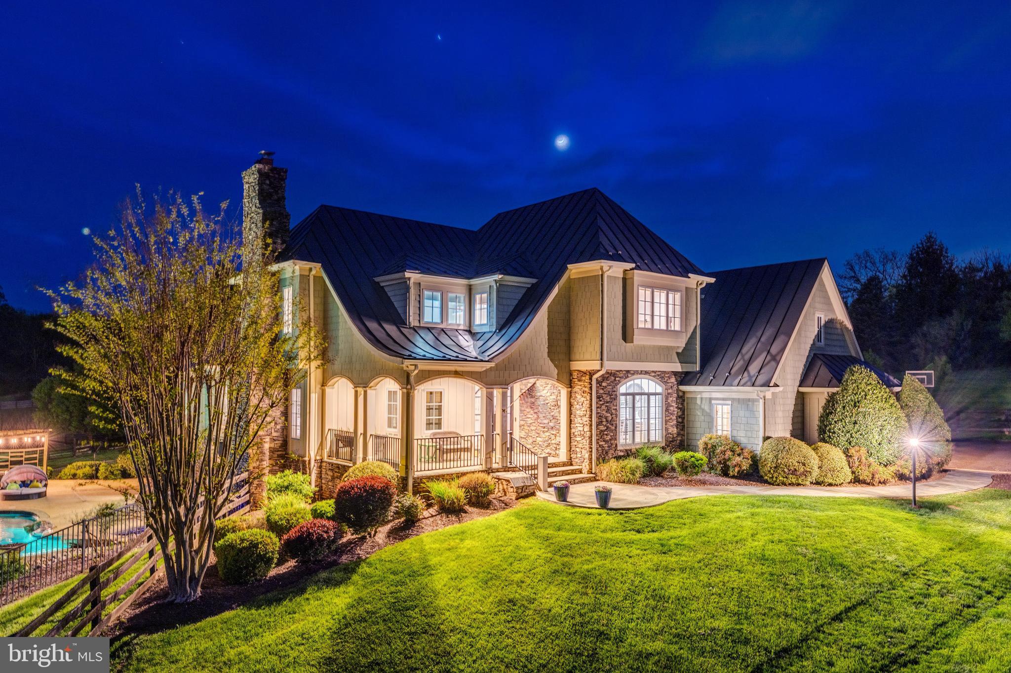 Welcome to Skyfall, a custom-built modern farmhouse thoughtfully designed with the finest materials, exuding sophisticated luxury on 9.08 meticulously fenced acres secured by private electric-gate access. Nestled on prestigious Peale Lane—a secluded enclave celebrated for estate-quality homes amid Loudoun County’s picturesque wine country—Skyfall offers exceptional privacy, yet is mere minutes from vibrant downtown Leesburg. Crafted with impeccable attention to detail, the home's striking entry features imported black French steel doors beneath a dazzling Schonbek German crystal chandelier, accented by tray ceilings and crown molding throughout the main level. Durable Hardi-plank siding, a sleek full metal roof, and new Carrier HVAC systems with UV technology underscore the superior quality of construction. The luxurious main-level primary suite includes dual walk-in closets, French steel doors, and a cozy sitting area with a Jotul wood stove surrounded by marble. Its opulent ensuite bath features reclaimed barn doors, cathedral-arched windows, an oversized Kohler soaking tub, Toto Japanese toilet, dual Indian marble vanities, and frameless rainfall shower. Two chic powder rooms—including one concealed within the laundry—ensure convenience. Ascend the dramatic waterfall staircase to three spacious bedrooms, each with generous walk-in closets. One bedroom has a private ensuite bath with marble vanity; the other two share a Jack-and-Jill bathroom with dual Carrera marble vanities, clawfoot tub, and seamless glass shower. A charming reading nook completes the upper level. The gourmet kitchen impresses with expansive floor-to-ceiling cabinetry, waterfall quartz island with cabinetry on both sides and integrated power, WiFi-enabled Thermador appliances including discreetly integrated fridge, freezer, dishwasher, wine fridge, 6-burner range with griddle, twin ovens and integrated Chef's hood.. Under-cabinet lighting, hidden outlets, and a trough sink with dual faucets enhance functionality. An adjacent hidden pantry mirrors kitchen finishes with quartz counters and open English oak shelves, and handmade hickory barn door entrance. The expansive family room features soaring cathedral ceilings, exposed wood beams, rustic stone fireplace insert, built-in English oak workspace, and access to the wraparound porch. A formal dining room, illuminated by a statement fixture, is perfect for entertaining. The finished lower level is an entertainer’s paradise, highlighted by a reclaimed Virginia barn wood bar with Indian marble, dishwasher, EuroCave wine fridges, beer fridge, and sink. A stacked stone fireplace with Jotul stove warms the rec room, while a hidden theater/music room lies behind a custom bookcase. A guest suite with reclaimed wood vanity and full bath, fitness room, workshop, and ample storage offer additional comfort, all with direct access to the pool deck. The outdoor haven centers around a stunning 30,000-gallon PebbleTech gunite pool, tanning ledge, 8–10-person spa, and impressive 11.5-ft deep end, that slopes to a swallower end.. Exterior amenities include a Trex deck, flagstone patio with Jotul fire pit, and stone-enhanced pool deck. Custom artisan electric gates by Aurora Services on Virginia bluestone columns feature AES PRO smart-device control. Equestrian facilities include a pristine 4-stall barn with new metal roof, hot/cold water, tack room, hayloft, and adjoining 7-acre fenced paddock. Facing nearly due south, Skyfall feels secluded and serene yet is conveniently situated only minutes from Dulles Airport and within easy driving distance of Washington, DC. Located just 4.6 miles from historic Leesburg with quick access to Route 15, the Greenway, over 50 wineries and breweries, and scenic trails including the Appalachian Trail, Skyfall represents a rare opportunity to experience refined craftsmanship and luxurious comfort in Northern Virginia’s most desirable countryside setting.