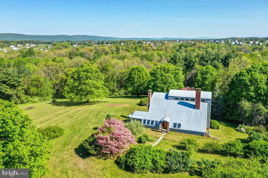 Welcome to your new and amazingly scenic, private 20-acre retreat, nestled in the midst of a countryside rich with history. A large piece of land is hard to find, especially one with such gorgeous views of the Blue Ridge Mountains. You’ll admire the tree-lined driveway as you make your way onto the property.  Enter the home, and you’ll immediately notice the freshly painted walls and trim. To the right of the entry foyer there is a south-facing bedroom with sunny windows gracing the ceiling and wall. Across the hall, a larger set of windows, and wood-beamed ceiling standout in the dining room. French doors separate the dining room from the sunroom, which is highlighted by its unique ceiling structure. It also has a door to the outside and brand new windows wrapping around the room with views of the yard. A laundry nook is on the main floor, with appliances under five years old. The kitchen has stainless steel appliances, including a brand new stove and dishwasher, and newer refrigerator. Cooks rejoice with the pantry closet! The main level of the home also has an office, full bathroom, and unfinished utility/storage area. The heart of the home is the living room, a uniquely impressive place. Towering windows flood the room with sunlight. Wooden columns, beams and panels surround the vast two-story space. A considerably sized wood-burning fireplace is another highlight. Sliding glass doors provide access to the freshly painted back deck, where mountain views abound. New carpet covers the stairs leading to the upper level with a second full bathroom, and two bedrooms. Recessed lights are in the bedrooms, and brand new hardwood floors exist upstairs, and throughout much of the main level. There is also a large storage area upstairs, and the hallway loft provides a fantastic view of the living room. There’s also an unfinished basement. This home was originally designed for an artist who did many of the stained glass windows at the National Cathedral in Washington D.C. The lot is primarily wooded and slopes toward the North Fork Catoctin Creek. About two to three acres of the land include the house, an inground pool, and a garage with a loft serving as an outbuilding on the property. Opportunities exist to get creative with this portion, potentially building out a garden or guest house. This picturesque 20-acre site is located just off the intersection of Charles Town Pike and Berlin Turnpike, north of Leesburg and Purcellville, and outside of historic Waterford. The area is a scenic getaway, especially for wine and brewery enthusiasts and those desiring a stay at a local bed & breakfast. Catch the Metro train at Moorfield Station (20 miles) which goes into Washington D.C. or take a flight from Dulles Internationa Airport (25 miles).