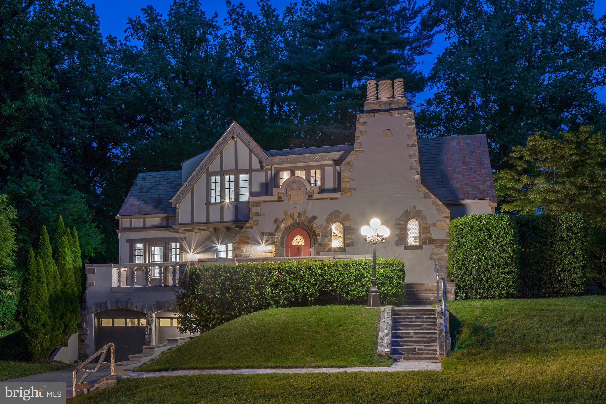 With the bold inscription "Cedere Numquam" (Never Give Up) carved in stone above the front door, this striking Tudor-style home invites you into a world of timeless elegance and thoughtful design. Originally built in 1923 and expanded with care, it seamlessly blends classic architecture with modern additions and design.
Perched on a quiet cul-de-sac above Sligo Creek Park, the stone-and-stucco exterior is enhanced by welcoming stone walkways and sculptural metal railings by Barton Rubenstein. A custom wood door opens to reveal a dramatic great room with a 20-foot beamed ceiling, a stone fireplace, a floating glass display wall by Renwick curator Michael Monroe, and soaring atrium windows framing the private garden terrace.
The banquet-sized dining room features a coffered ceiling with a custom crest of The Order of the Garter, a nod to tradition that echoes the home's enduring character. The adjacent kitchen offers granite countertops, ample cabinetry, and a breakfast area that flows into the cozy family room with an 1800s Great Western cast iron parlor stove.
The main-level owner's suite is a true retreat, with two oversized walk-in closets, two beautifully appointed full baths, and a grand bed chamber with French doors leading to the terrace. A second office or nursery adds flexibility with an additional walk-in closet.
All baths on the main level feature high-end Italian fixtures, and the owner's suite baths have heated floors & enormous walk-in showers.
On the upper level, a reading balcony/lounge overlooks the great room, alongside three additional bedrooms—including a suite with sitting room/den—and two full baths. Two spaces have built-in window seats, and the 3rd bedroom features built-in furniture. The lower level provides space for hobbies, storage, and access to the deep 2-car garage and elevator.
Recent updates include fresh interior and exterior paint, refinished hardwood floors, new carpet, and updated lighting. A whole-house generator is also installed. See Disclosures for additional information on systems and receipts.
The terraces and gardens, accessed through the great room, owner's suite, and family room, provide views and shade from the towering Japanese maple tree with its ever-changing colors. Privacy abounds, with access to Sligo Creek Park from a corner of the yard. A sprawling front lawn greets guests with an impressive approach and offers plenty of play space both front and back.
Walkable to Zinnia and convenient to Metro, buses, and I-495, this timeless home offers rare character, comfort, and presence—ready for its next chapter.