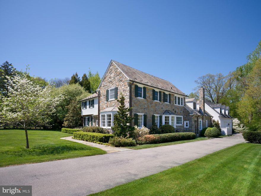 Set at the end of a Wynnewood cul-de-sac, surrounded by homes of similar scale and character, this stone Colonial draws equal strength from its setting and its architecture—expanded through an executed addition by EB Mahoney Builders that preserves the proportions and craftsmanship of the original home while delivering the space and flow expected today.

A vestibule entry opens to a traditional center-hall plan with hardwood floors throughout. The wood-paneled library, anchored by a fireplace and served by its own powder room, connects to a sunroom wrapped in stone and beadboard—a light-filled space that also opens to the living room and kitchen, establishing a natural flow across the main level. The living room, with a second fireplace and windows on multiple exposures, sits opposite a formal dining room, where a deep bay window frames views of the front grounds and mature specimen trees.

At the center of the home, the kitchen—reworked as part of a later renovation—is anchored by an expansive center island with seating, complemented by full-height custom cabinetry and a bright breakfast area. The space opens directly to the sunroom and adjoining family room, reinforcing the flow of the main level and supporting both everyday use and entertaining. A mudroom, second powder room, and access to the oversized garage complete this level.

Upstairs, a central landing leads to a private primary suite with a walk-in closet and double-vanity bath. Four additional bedrooms and three baths complete the second floor with a well-balanced layout.

The lower level is filled with natural light from oversized window wells and features a stone fireplace along with custom built-in desk workspaces, creating a flexible area for work, study, and everyday use. Storage and mechanical spaces are substantial and well organized.

A flagstone terrace overlooks broad, level rear grounds—uncommonly usable space suited for sports, play, and larger-scale outdoor living. The home has been extensively improved and consistently maintained over time, with a comprehensive addition, subsequent renovations, and significant landscaping and hardscaping enhancements.

Ideally located in Lower Merion Township, with convenient access to Suburban Square, regional rail, and Center City.