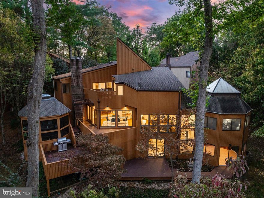 Discover the perfect blend of architectural artistry and modern luxury in this Frank Lloyd Wright–inspired mid-century contemporary tucked into the natural beauty of Hobbit’s Glen—one of Columbia’s most coveted settings. Designed to harmonize with its wooded surroundings and backing to preserved Patapsco parkland, this residence offers a lifestyle defined by creativity, comfort, and connection to nature. The main level welcomes you with light-filled spaces, custom hardwood kitchen cabinetry, massive center island, and custom countertops, complemented by custom luxury vinyl flooring. A true culinary centerpiece, the kitchen features Sub-Zero refrigerator and beverage fridge, Gaggenau stovetops, dual indoor grills, dual ovens, and dual Fisher & Paykel dishwasher drawers—a chef’s dream in form and function. Gather in the expansive family room with wood-burning fireplace, or work from home in the sunroom/office appointed with a bespoke wood-paneled ceiling, and custom library shelving. The home’s thoughtful upgrades continue with recessed LED lighting (2024), Lutron smart switches (2024), three-zone Ecobee climate control, dual radon mitigation systems (one new 2024/25), and Vivint home security system. Upstairs, the primary suite impresses with vaulted ceilings, a spa-like bath, and a private roof deck creating a serene treetop retreat. Three additional bedrooms complete the level, including one two-story suite with a spiral staircase. The walkout lower level offers abundant storage—two+ rooms with custom shelving—and access to the stunning outdoor living area. Enjoy three levels of decking with comprehensive architectural lighting, or relax in the screened-in gazebo, built on a slab foundation with electric lighting, skylights, full roof, and hidden storage below. Energy-efficient highlights include Level 2 EV charging, a 400-amp electrical panel, heat pump water heater, and architectural shingle roof constructed with 14 off-center framing for strength and design integrity. Moments from Columbia’s network of walking paths, playgrounds, and Hobbit’s Glen Golf Course, this one-of-a-kind residence combines inspired architecture, high-performance living, and a tranquil natural backdrop—all within reach of the best village amenities.