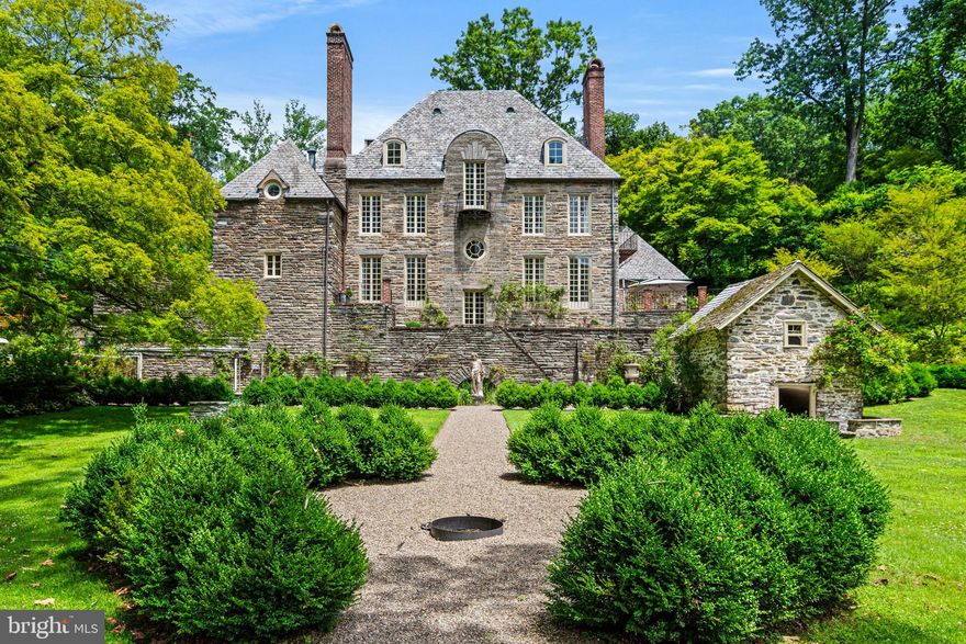 The Firs, a Normandy-style residence by George Howe, stands behind stone gates and cobblestone drive, surrounded by curated gardens and centuries-old trees—a rare architectural jewel in Chestnut Hill. Brick terraces, stone patios, and garden paths connect a succession of outdoor ‘rooms,’ each offering its own vantage point for gatherings or quiet retreat. Here, privacy meets convenience: trail access to Fairmount Park is just beyond the garden gate, while Chestnut Hill’s village shops, cafés, and train to Center City are minutes away.
Inside, original architectural details speak to the home’s pedigree—Yellin wrought-iron work graces the staircase, light fixtures, and hardware, while hand-carved stone and wood fireplace mantels, crown molding, random-width hardwood floors, and crystal door handles provide enduring character throughout.
The living room centers around a carved rose granite and wood fireplace, with floor-to-ceiling windows that invite natural light and open through French doors to a sweeping brick terrace overlooking the grounds—ideal for entertaining. The formal dining room, accented by a gas fireplace and coffered walls, offers French doors to a charming patio balcony. The kitchen features original butler’s pantry cabinetry, a center island, gas range, Sub-Zero refrigerator, and a sunny breakfast area with bay window overlooking a private courtyard and kitchen garden. A marble powder room, private study, and second rear staircase complete the main level.
Upstairs, the primary suite is a serene retreat with views of the rear gardens, a wall of closets, and a luxurious marble bath featuring dual vanities, a walk-in shower, and a soaking tub with picturesque garden view. A library with built-in shelving, two additional bedrooms, a marble hall bath, and a laundry room complete the second floor. The home’s baths have been thoughtfully renovated, blending timeless materials with modern comforts to complement the home’s historic character. The third level offers three more bedrooms and a generous cedar closet. The walkout lower level offers a sauna, gym, and ample storage space.
The property’s patios, gardens, and meandering paths set it apart—designed to be enjoyed from nearly every window. A long gravel walk leads past curated gardens and specimen trees, while a hidden side path connects directly to Fairmount Park’s extensive trail network. Offering both privacy and proximity, this distinguished residence is convenient to Chestnut Hill, Manayunk, major roadways, and the train. A rare offering in one of Philadelphia’s most special locations.