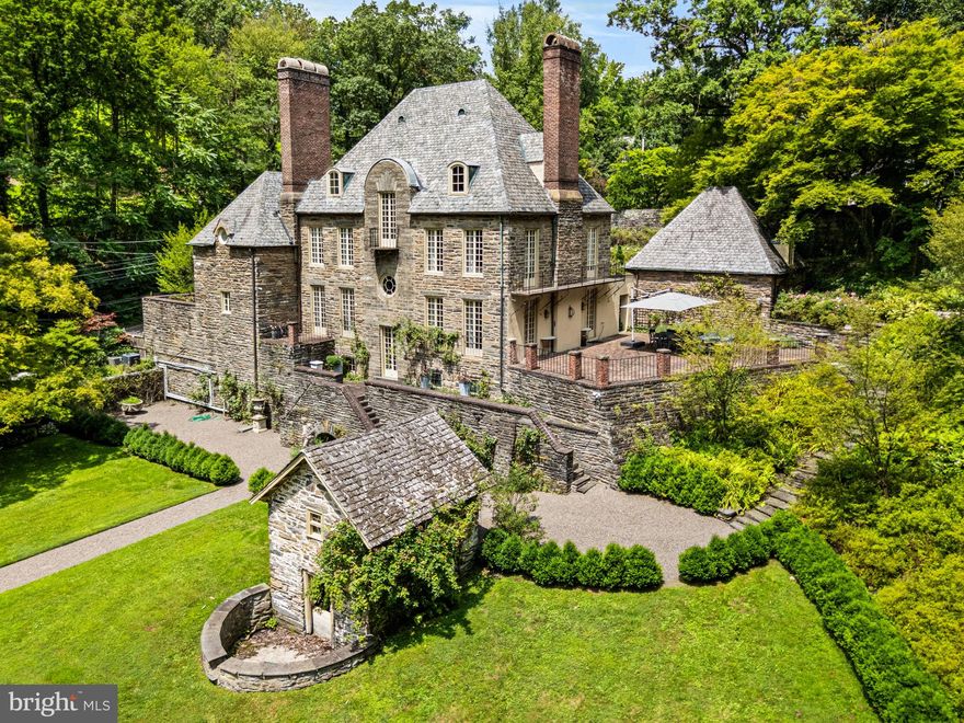 The Firs, a Normandy-style residence by George Howe, stands behind stone gates and cobblestone drive, surrounded by curated gardens and centuries-old trees—a rare architectural jewel in Chestnut Hill. Brick terraces, stone patios, and garden paths connect a succession of outdoor ‘rooms,’ each offering its own vantage point for gatherings or quiet retreat. Here, privacy meets convenience: trail access to Fairmount Park is just beyond the garden gate, while Chestnut Hill’s village shops, cafés, and train to Center City are minutes away.
Inside, original architectural details speak to the home’s pedigree—Yellin wrought-iron work graces the staircase, light fixtures, and hardware, while hand-carved stone and wood fireplace mantels, crown molding, random-width hardwood floors, and crystal door handles provide enduring character throughout.
The living room centers around a carved rose granite and wood fireplace, with floor-to-ceiling windows that invite natural light and open through French doors to a sweeping brick terrace overlooking the grounds—ideal for entertaining. The formal dining room, accented by a gas fireplace and coffered walls, offers French doors to a charming patio balcony. The kitchen features original butler’s pantry cabinetry, a center island, gas range, Sub-Zero refrigerator, and a sunny breakfast area with bay window overlooking a private courtyard and kitchen garden. A marble powder room, private study, and second rear staircase complete the main level.
Upstairs, the primary suite is a serene retreat with views of the rear gardens, a wall of closets, and a luxurious marble bath featuring dual vanities, a walk-in shower, and a soaking tub with picturesque garden view. A library with built-in shelving, two additional bedrooms, a marble hall bath, and a laundry room complete the second floor. The home’s baths have been thoughtfully renovated, blending timeless materials with modern comforts to complement the home’s historic character. The third level offers three more bedrooms and a generous cedar closet. The walkout lower level offers a sauna, gym, and ample storage space.
The property’s patios, gardens, and meandering paths set it apart—designed to be enjoyed from nearly every window. A long gravel walk leads past curated gardens and specimen trees, while a hidden side path connects directly to Fairmount Park’s extensive trail network. Offering both privacy and proximity, this distinguished residence is convenient to Chestnut Hill, Manayunk, major roadways, and the train. A rare offering in one of Philadelphia’s most special locations.