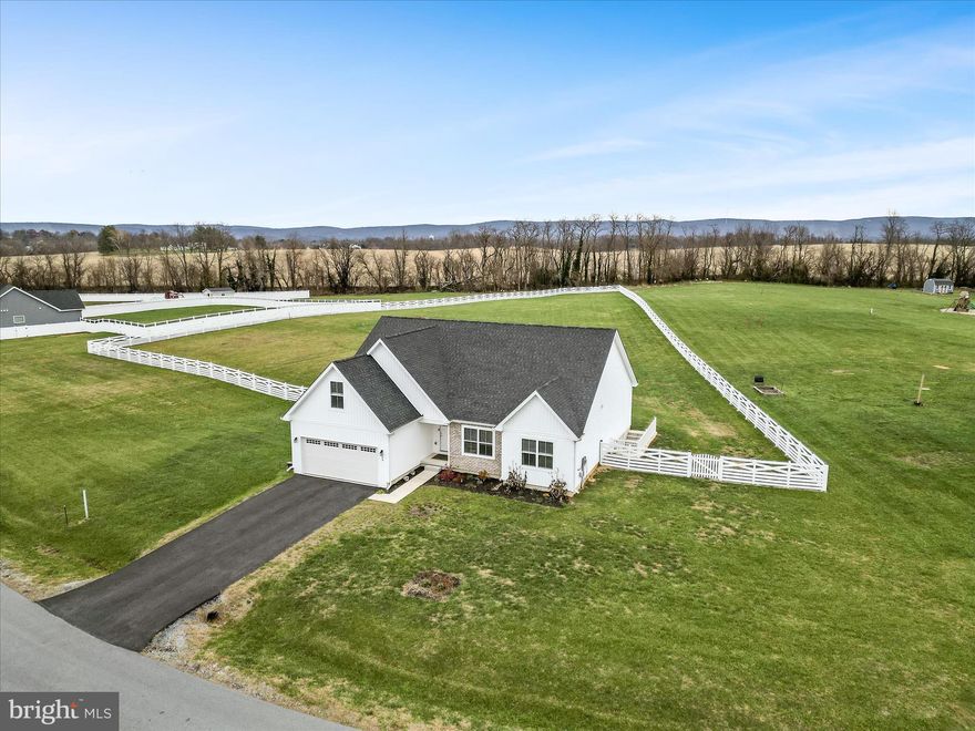 This 2022 ranch-style home offers 4 bedrooms and 3 full baths which sits on 1.66 acres, one of the most generous lots in Milton’s Landing, a community known for its spacious one-acre-plus homesites and its close proximity to historic Charles Town, WV-340, and MD-15. The interior is open and bright, beginning with vaulted ceilings and detailed wainscotting that define the main living area. The kitchen serves as the central hub, outfitted with white cabinetry, granite counters, stainless steel appliances, and a substantial island that doubles as a workspace and gathering spot. The living room includes a fireplace and looks out over the expansive backyard, with luxury vinyl plank flooring tying the entire main level together. The primary suite is positioned for privacy and includes a custom-shelved walk-in closet and a spacious bath with a dual vanity and soaking tub. Two more main-level bedrooms share a full hall bath, while the upper-level loft offers an additional suite complete with its own bedroom, closet, and full bath—ideal for guests. A dedicated laundry room is also located on the main level. The home provides 2,045 finished square feet above grade, with the opportunity to bring the total to more than 3,800 square feet by finishing the full, insulated walk-out basement, which already features rough-in plumbing, a sliding door, and a walk-up to the backyard. Rounding out the property are a two-car garage with paved driveway, a whole-house water filtration system, and a generous fenced backyard ready for gardening, recreation, or future outdoor amenities.