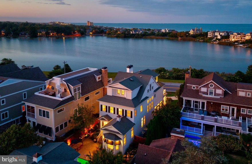 Introducing 20418 Silver Lake Drive, an extraordinary coastal retreat affectionately known as “High Pointe.” Perfectly positioned along the shores of Silver Lake in Rehoboth Beach, this 6-bedroom, 6.5 bath residence commands one of the most desirable vantage points in town, where sparkling lake views meet glimpses of the Atlantic Ocean. The home’s shingle-style exterior, awnings, lush gardens, and multiple porches and decks create a timeless curb appeal. Offering more than 4,600 SF of interior living space, complemented by over 1,000 SF of outdoor living areas and an unfinished basement, High Pointe balances elegance with functionality. Step inside and experience a remarkable blend of classic detail and fresh, modern updates. A grand foyer with 12-foot ceilings and polished marble floors welcomes you and flows into the newly reimagined main living room. Designed with a contemporary edge, this space showcases a dramatic floor-to-ceiling wine storage cabinet, walls of windows, coffered ceilings, and a gas fireplace. Adjacent lies the dining area and a chef’s kitchen that has been completely renovated with sleek custom cabinetry, commercial-grade appliances, and beautiful quartz countertops. The first level also includes a bright guest suite, a versatile laundry room that doubles as a butler’s pantry, a stylish powder room, and a screened porch overlooking the private backyard. A graceful staircase lined with oversized windows leads to the second floor, where built-ins and a personal library define the landing. The waterfront primary suite has been transformed into a spa-like escape, featuring dual walk-in closets, a sitting area, and a fully updated ensuite bath with sophisticated finishes that evoke the luxury of a 5-star hotel. This level also offers two additional guest suites with private baths. On the top floor, a relaxed lounge opens to a sun deck with sweeping lake and ocean vistas. A fifth bedroom with ensuite bath and dual closets and an additional finished walk-in closet is ideal for extra storage. For ultimate ease, an elevator services every floor, including the spacious unfinished basement that offers room for expansion. The outdoor setting is every bit as impressive as the interiors. Manicured landscaping, irrigation, and a heated saltwater pool are accented by a paver patio, outdoor shower wrapped in wisteria, landscape lighting, surround sound, and tranquil water features – creating the perfect backdrop for summer entertaining. An oversized two-car garage provides ample parking and storage, while above it, a charming one-bedroom guest apartment offers its own kitchen, living area, laundry, and full bath. Offered fully furnished, this home presents a rare opportunity to own a turn-key coastal estate in Rehoboth Beach, ready to be enjoyed for the 2026 summer season.