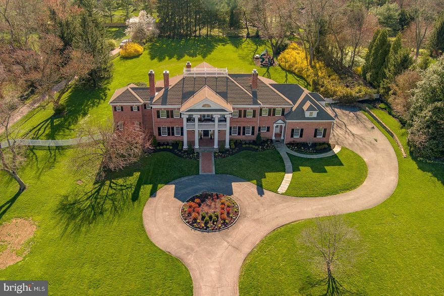 Step into the grand foyer of this Georgian-style home and be greeted by the warm embrace of traditional elegance seamlessly blended with modern luxury. Recently featured in Traditional Home Magazine alongside renowned interior designer Glenna Stone, this nearly 9,000-square-foot estate overlooks Philadelphia Country Club in the coveted Gladwyne neighborhood, a true suburban oasis.
As you enter through the arched doorway, the great room beckons with its 28-foot-high wood trusses and beams, infusing the space with a sense of comfort and sophistication. Expansive windows and French doors invite the outdoors in, offering breathtaking views of the surrounding landscape.

A graceful curved staircase leads to a circular landing and balcony on the upper level, creating an ideal setting for entertaining against the backdrop of the picturesque golf course. The dining room, adorned with a painterly emerald green silk wall covering and a cozy fireplace, exudes an elevated charm perfect for intimate gatherings. Tucked behind pocket doors, the living room strikes a balance between formality and comfort, boasting exquisite molding, built-in bookshelves, and a marble fireplace.The fully remodeled kitchen is a vision of contemporary elegance, featuring Giotto quartzite countertops, an oversized island, and slate blue cabinetry bathed in natural light. This level also offers a spacious powder room with unique tile flooring and brass accents, while a sun-soaked home gym and a vibrant, multifunctional office space cater to wellness and productivity.

The primary suite is a haven of luxury, complete with a cozy sitting area, a pass-through coffee bar, featuring a mini refrigerator and compact dishwasher that is perfect for enjoying a morning cup of coffee or a relaxing evening beverage without leaving the comfort of the suite. Indulge in a spa-like bathroom with heated tile flooring and a freestanding bathtub. Upstairs, two generously sized bedrooms each boast a fireplace and walk-in closet, sharing a large bathroom. A fourth bedroom features a beautiful bay window overlooking the expansive rear property, complemented by an en suite bathroom and walk-in closet. The fifth bedroom offers a private suite with its own ensuite bathroom, providing a serene retreat for guests or family members.

This exceptional home seamlessly marries traditional charm with modern comforts, creating an unparalleled living experience in one of Gladwyne’s most prestigious locations. Welcome to a timeless sanctuary where luxury and sophistication converge.