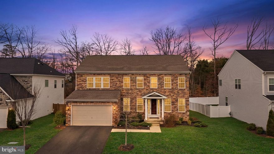 Some homes are built to shelter. This one was built to impress.
Nestled in Laurel Hills Crossing in Lorton, 8934 Hubbard Way is a stone-front colonial of rare distinction — 4,459 sq ft across three fully finished levels, with designer finishes, intentional architecture, and a lower level that redefines what it means to entertain at home.

EXTERIOR & CURB APPEAL
The all-stone facade sets the standard from the moment you arrive. A symmetrical colonial design, manicured landscaping, two-car garage, and gracious portico entry frame a home that commands attention at every hour — equally stunning at golden hour as under a twilight sky.

MAIN LEVEL · 1,528 SQ FT
The foyer opens to a soaring two-story family room anchored by a marble-surround fireplace, floor-to-ceiling sheers, and a statement staircase with dark wood treads and white balusters. Wide-plank luxury vinyl flooring runs throughout.

The gourmet kitchen is the showpiece: white shaker cabinetry with gold hardware, granite counters, gas cooktop, double wall ovens, French door refrigerator, stainless dishwasher, and a contrasting dark-base island under twin gold-and-crystal pendants. Breakfast nook and walk-in pantry complete the hub.
The formal dining room features designer wainscoting, crown molding, and a statement chandelier. A separate formal living room offers refined retreat with recessed lighting. A main-level in-law suite with private en-suite full bath delivers true single-level living for guests or family. Off the mud room, the bonus flex room — known as "the Costco Room" — features a built-in wrap-around wooden workspace with storage beneath. A powder room rounds out the floor. Custom Graber Blinds dress windows throughout the main and upper levels. Step outside to an 18' composite deck overlooking a private, wooded backdrop.

UPPER LEVEL · 1,513 SQ FT
The primary suite (16' x 23') is a true sanctuary — plush carpet, windows on two walls dressed in blackout Graber Blinds, a crystal fan chandelier, dual walk-in closets plus a third accessory closet, and a private en-suite featuring a designer-built three-head shower — the only one in the neighborhood. Three additional bedrooms share two full baths with granite vanities and dark espresso cabinetry. A dedicated upper-level laundry room adds daily convenience.

LOWER LEVEL · 1,418 SQ FT
This is where 8934 Hubbard Way separates itself from every other home in Northern Virginia.
The 34' x 22' main recreation room is an entertainer's dream — leather recliner sectional, wall-mounted TV, and a linear electric fireplace. The full wet bar is exceptional: white shaker cabinetry, granite counters, a peninsula with seating for four, stainless dishwasher, beverage refrigerator, and three tiers of open display shelving. A proper bar, built to host.

The 27' x 12' game room features a poker table, custom wine wall, and lounge sofa. A lower-level den with walk-in closet and adjacent full bath offers ideal guest accommodations. A private home gym completes the level — no membership required. Built-in Sonos speakers wire the entire lower level for sound.

COMMUNITY & LOCATION
One of Fairfax County's most desirable communities — tot lots, two pet relief areas, open green spaces, and the Laurel Hill Golf Club within the footprint. The Workhouse Arts Center, now home to Bunnyman Brewery, sits directly across the street. South Run Park, Occoquan Regional Park, and Laurel Hill Mountain Biking Trails provide year-round recreation.

Served by the South County pyramid — Silverbrook Elementary, South County Middle, and South County High — all highly rated within FCPS.

Direct access to I-95, Fairfax County Parkway, Route 123, and the Lorton VRE Station ( 3 miles). Fort Belvoir is minutes away. Springfield Town Center, Whole Foods, Trader Joe's, Wegmans, and Potomac Mills all within easy reach.